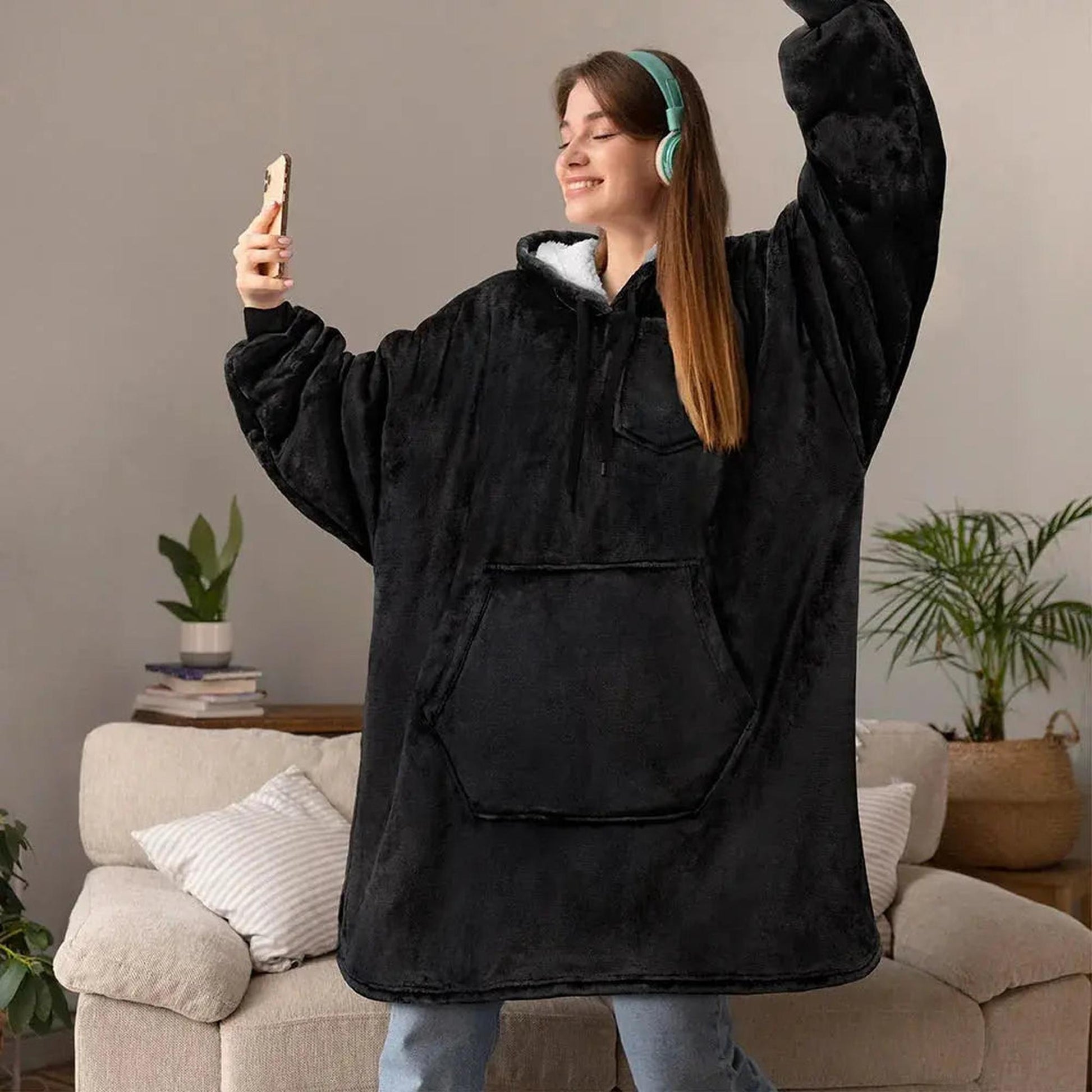 Smiling woman in an oversized black double fleece hooded jacket with a large front pocket, wearing headphones.