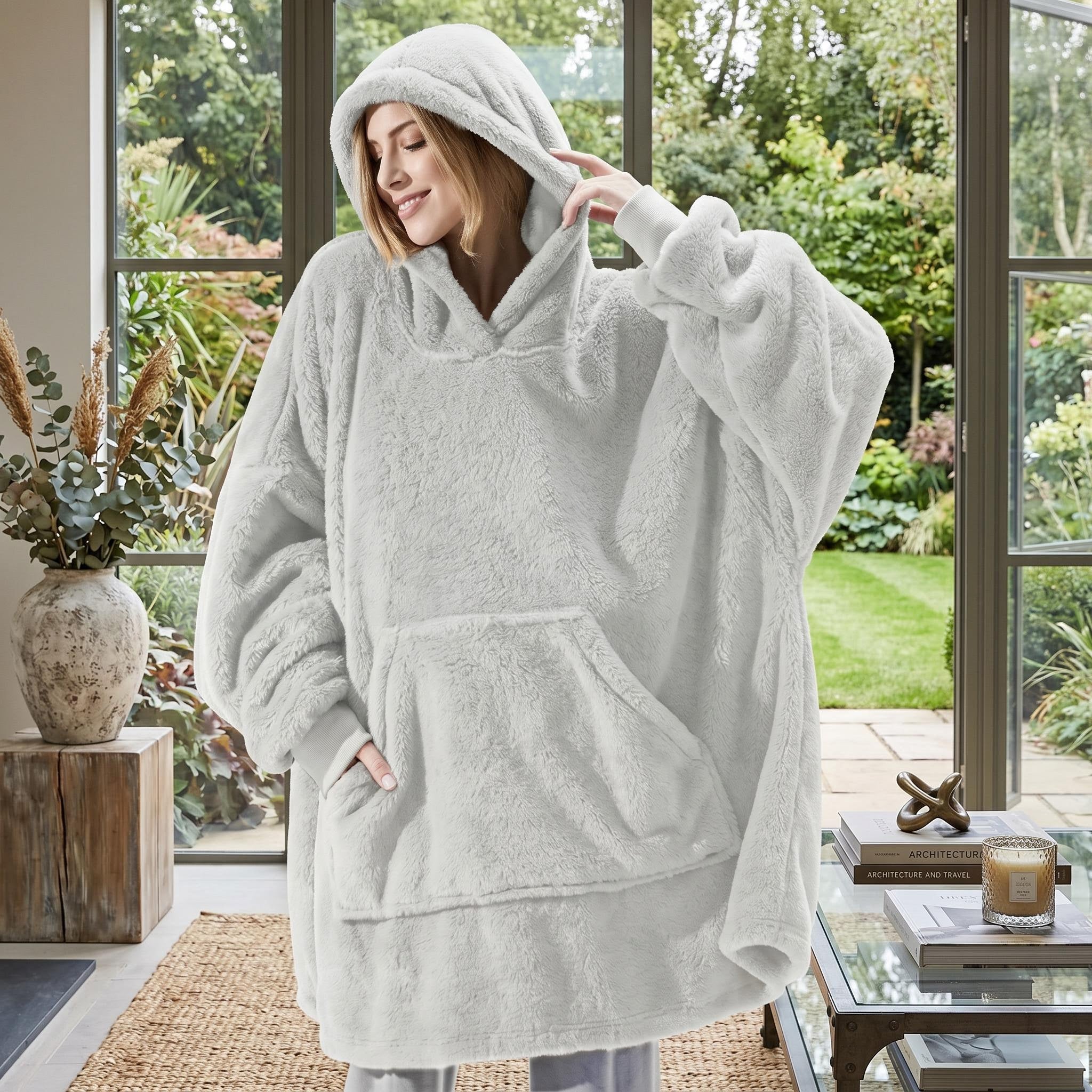 Woman in an oversized light grey double fleece hooded jacket with a large front pocket, smiling indoors.