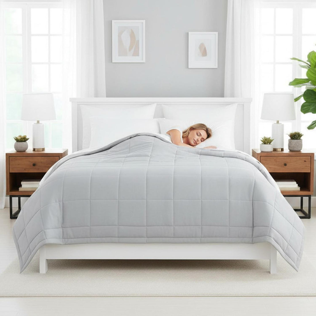 Light gray quilted down alternative blanket on a white bed with a woman sleeping peacefully.