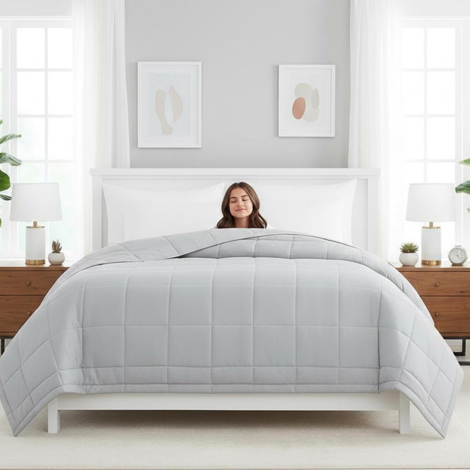 Woman sleeping soundly under a light gray quilted down alternative blanket on a white bed.