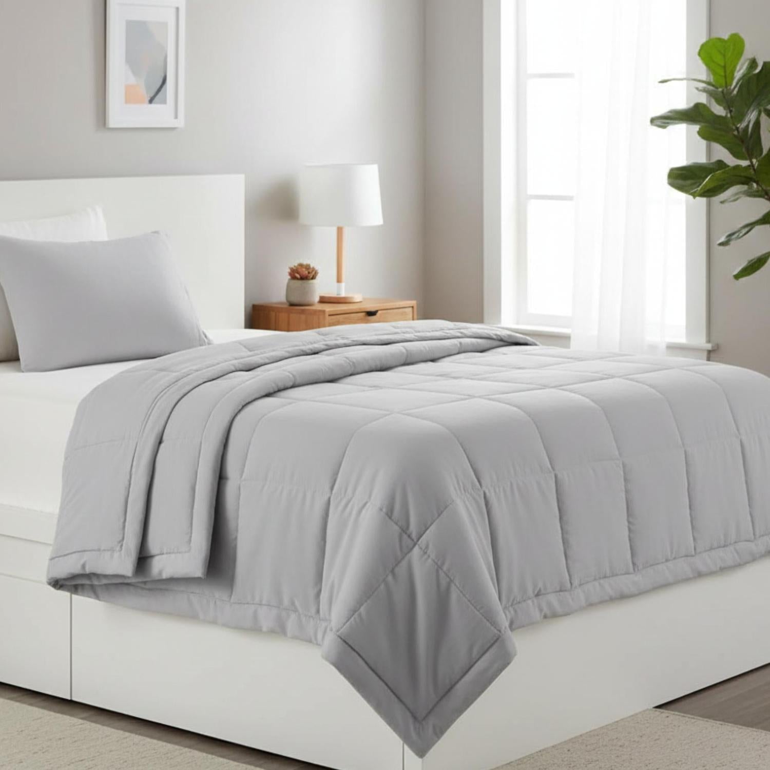 Light gray down alternative blanket quilt with embroidered square pattern on a white bed.