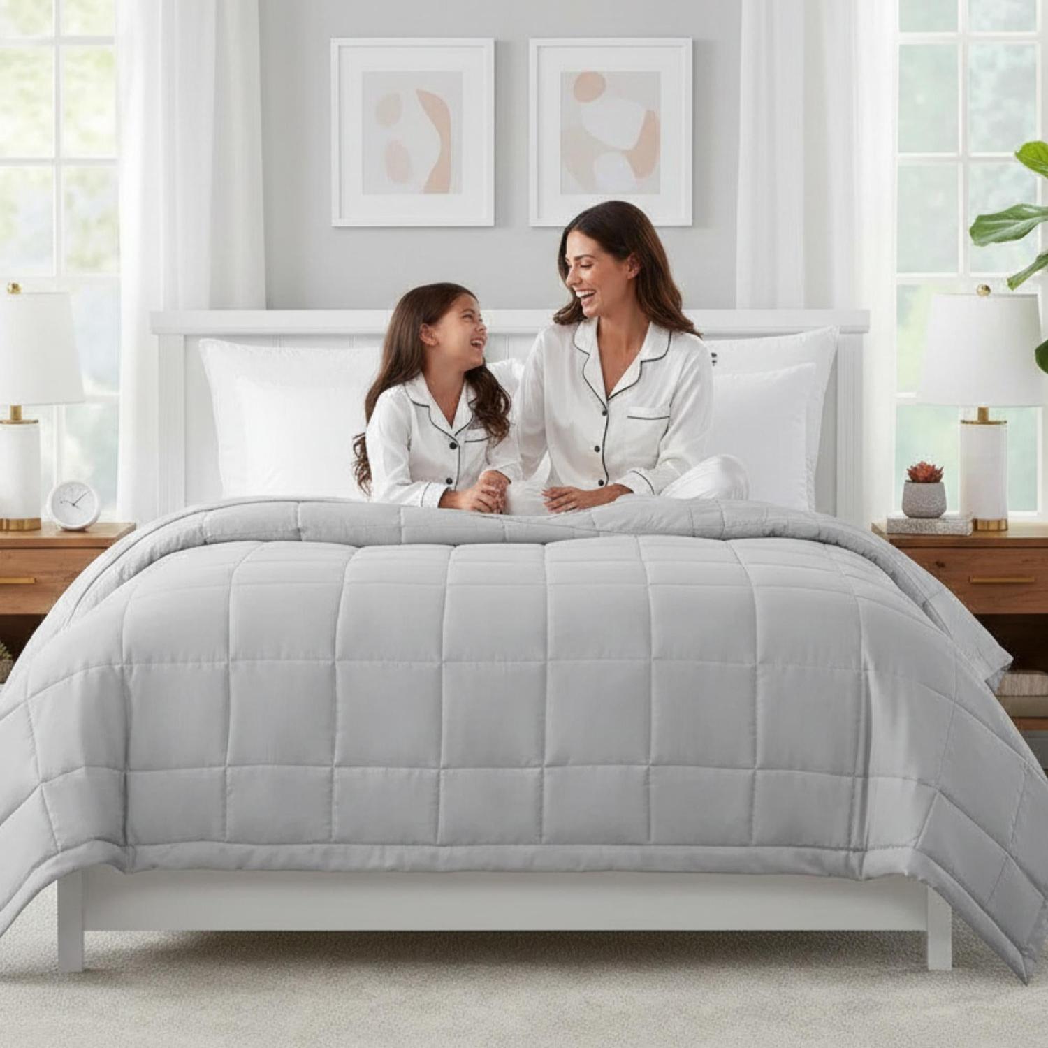 Mother and daughter on a bed with a light grey quilted down alternative blanket.