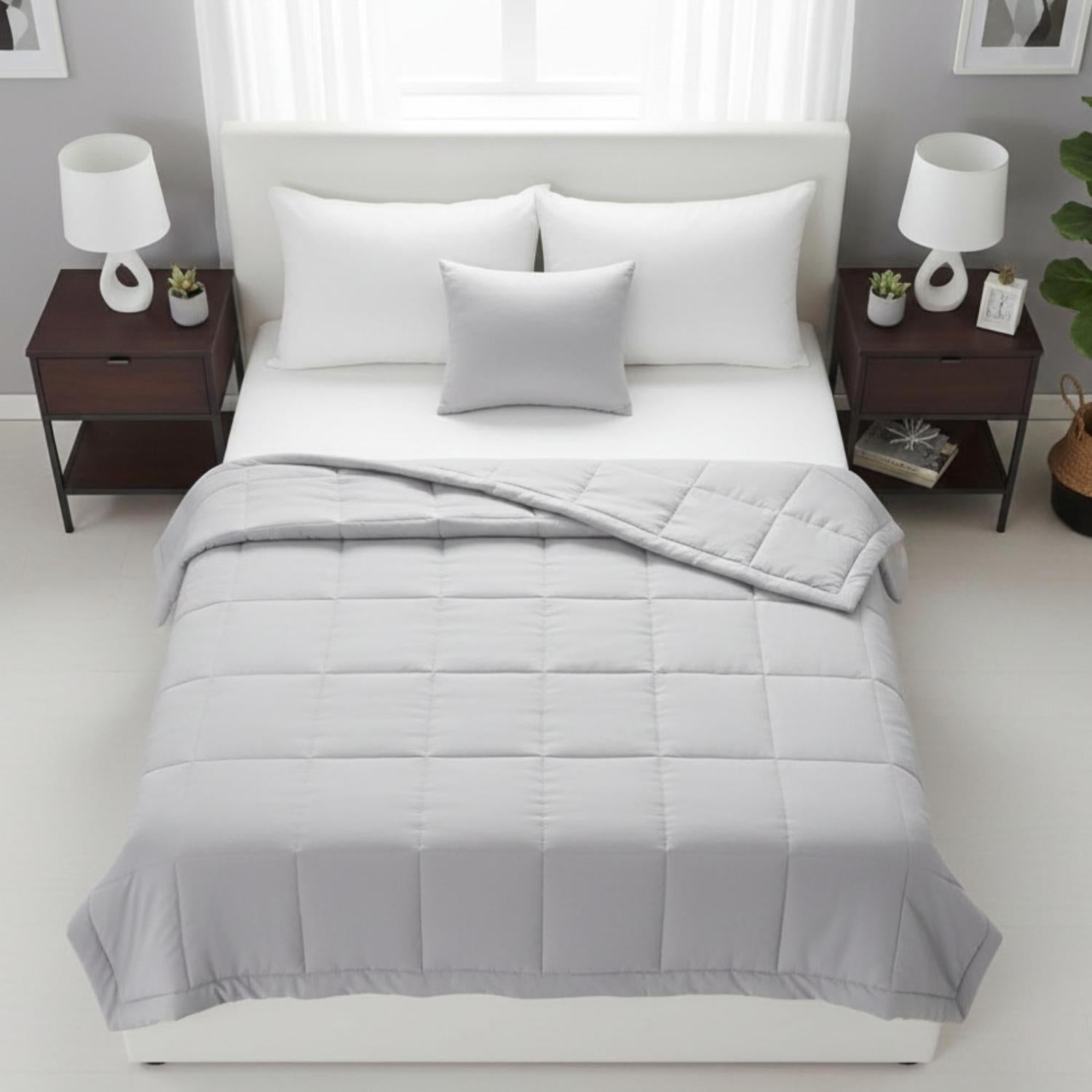 Light gray quilted down alternative blanket on a white bed with pillows.