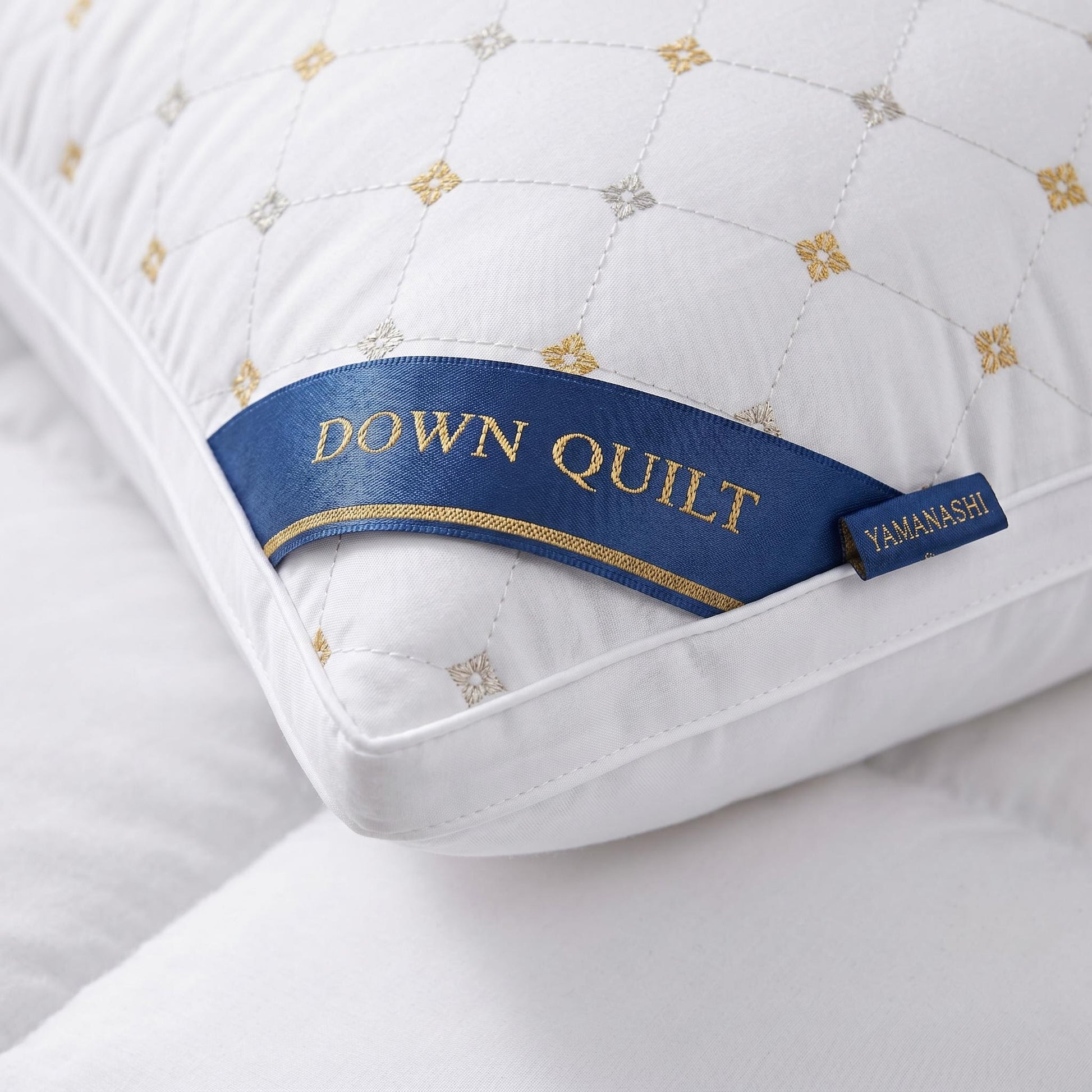 White quilted down alternative queen pillow with gold and silver embroidered pattern and blue "DOWN QUILT" label.