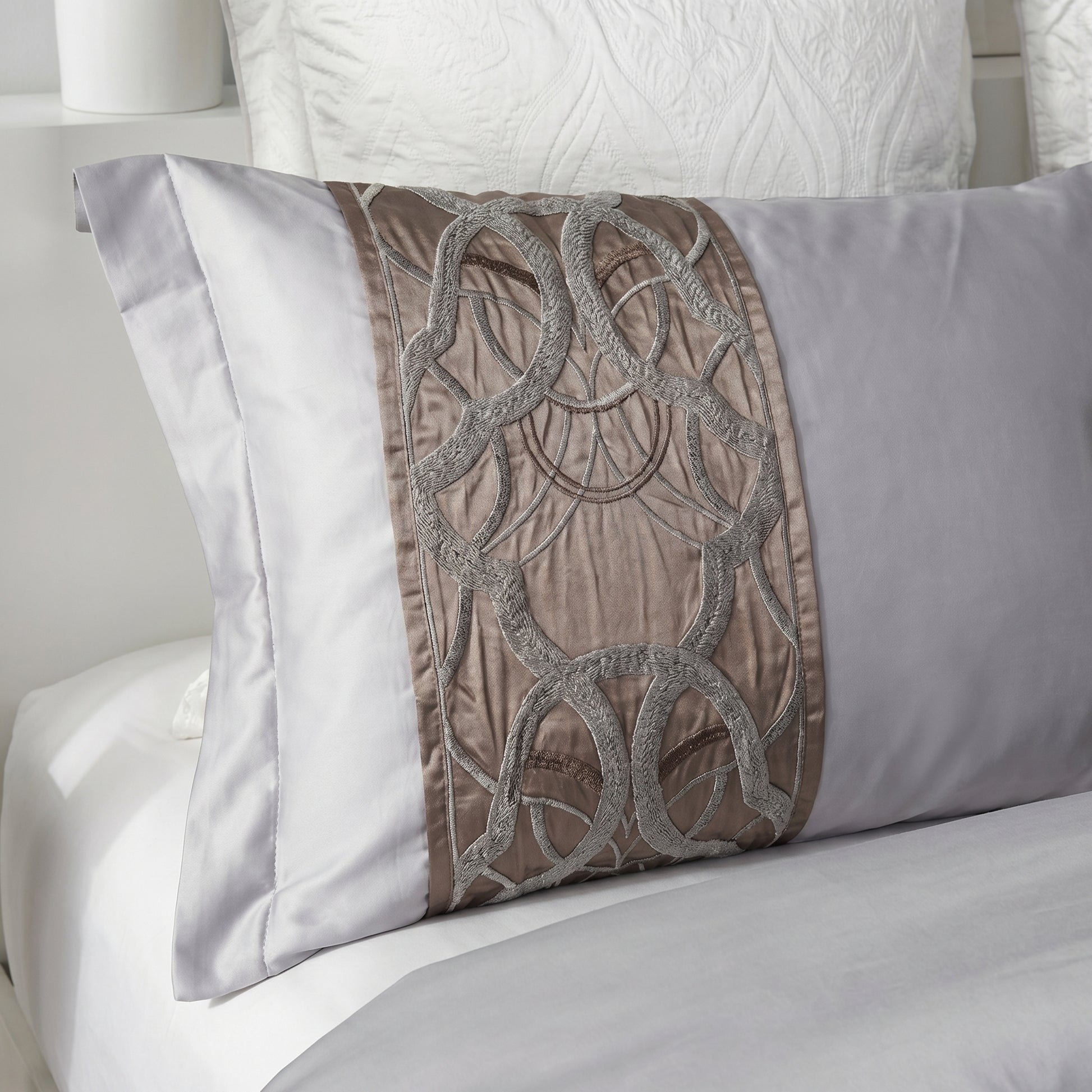 Elegant silvery-grey cotton pillow with intricate brown embroidered detailing, part of a bedding set.