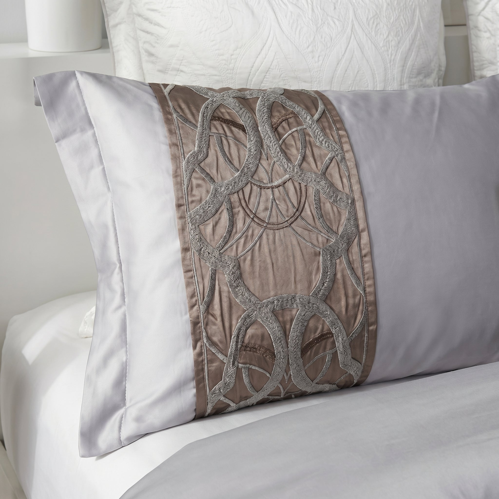 Elegant silvery-grey cotton pillow with intricate brown embroidered detailing, part of a bedding set.