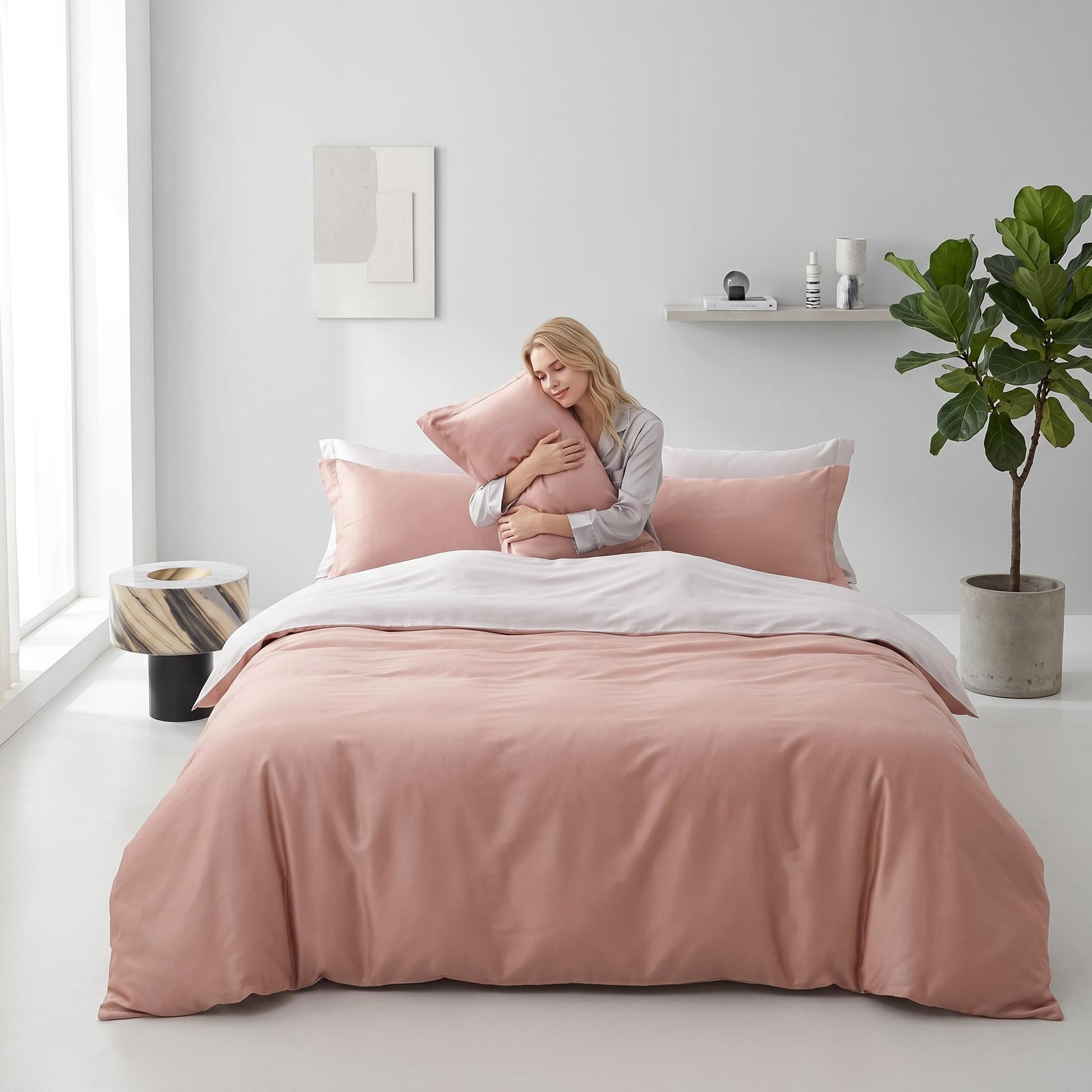Blonde woman hugging a pink organic cotton pillow on an elegant bed with a matching duvet cover.
