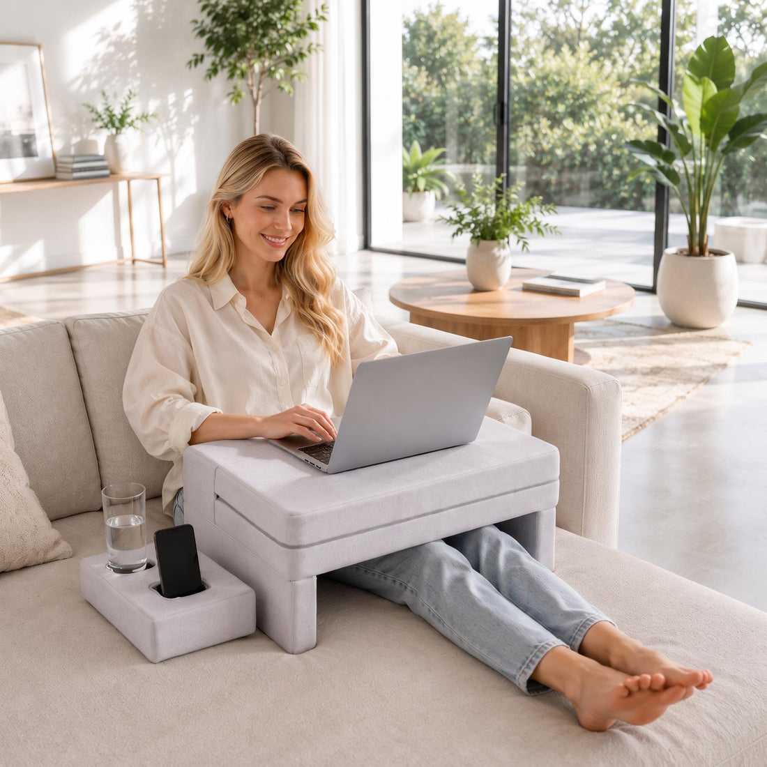 Woman using a grey ergonomic memory foam lap desk with armrest grooves and a phone holder while working on a laptop.