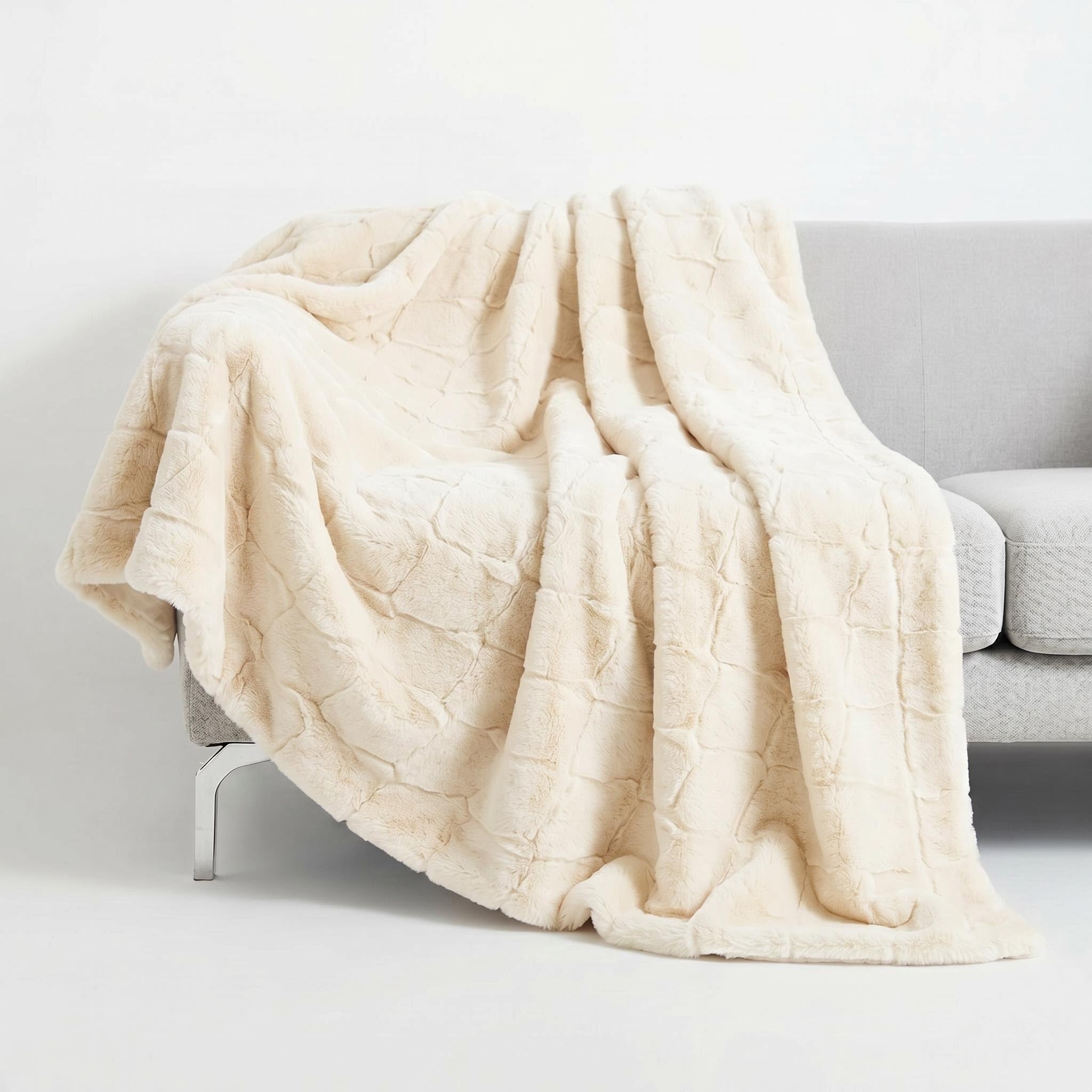Cream faux fur throw blanket with a subtle textured pattern draped over a gray sofa.