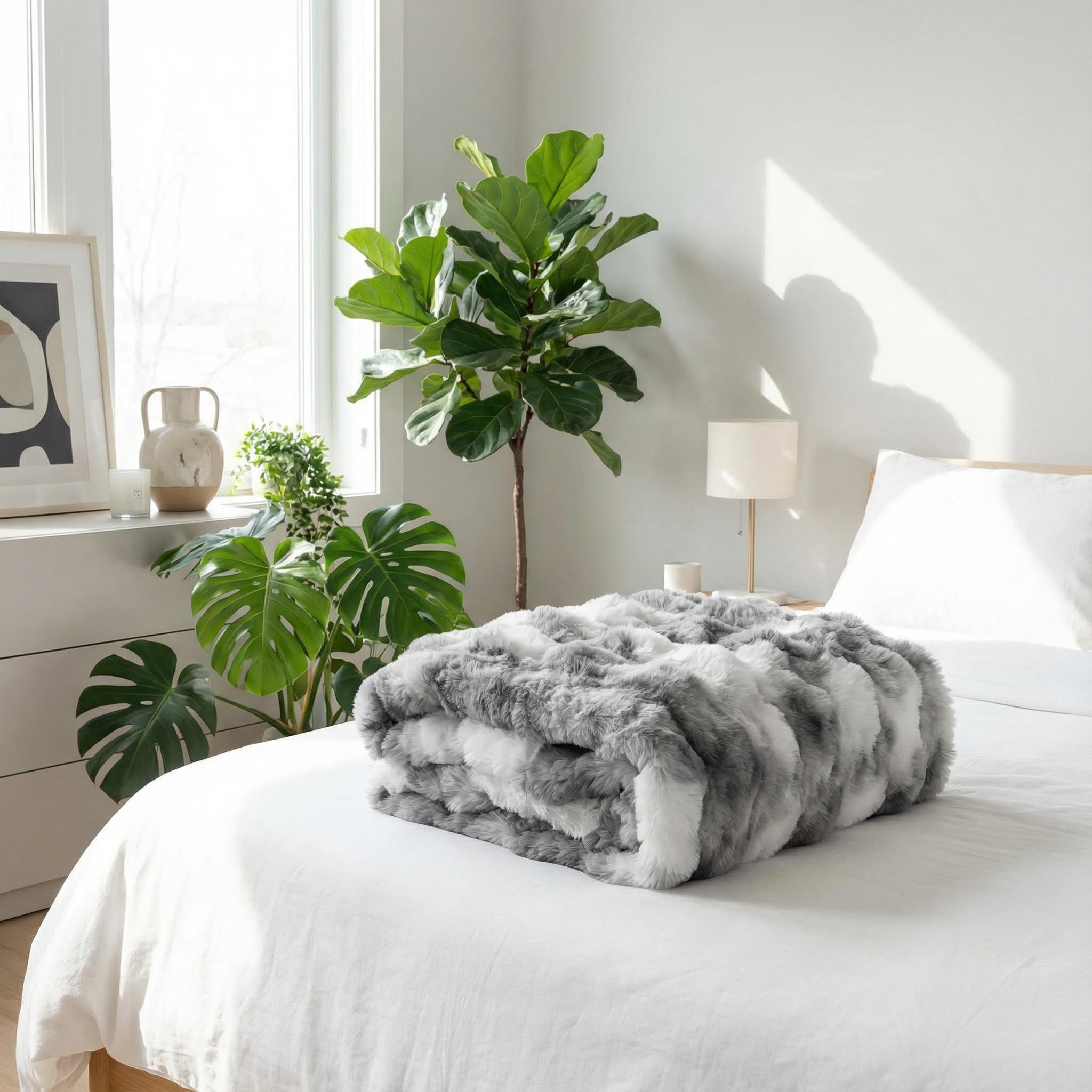Soft gray and white striped faux rabbit fur throw blanket folded on a white bed in a bright bedroom.
