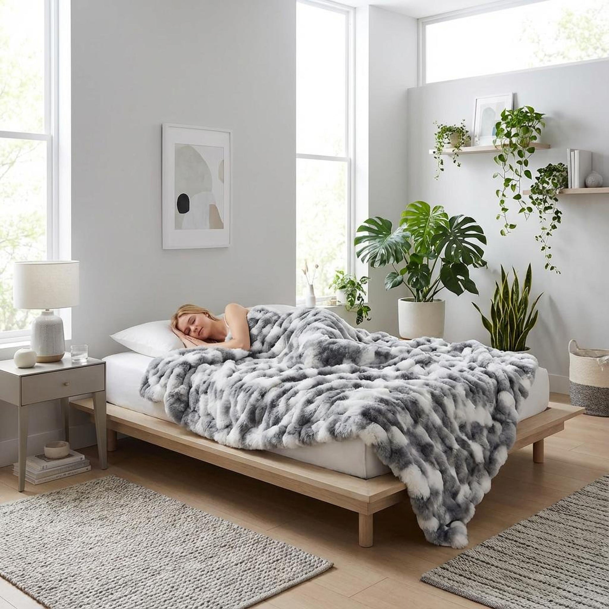 Woman sleeping peacefully under a soft, reversible gray and white faux rabbit fur throw blanket on a light wood bed.