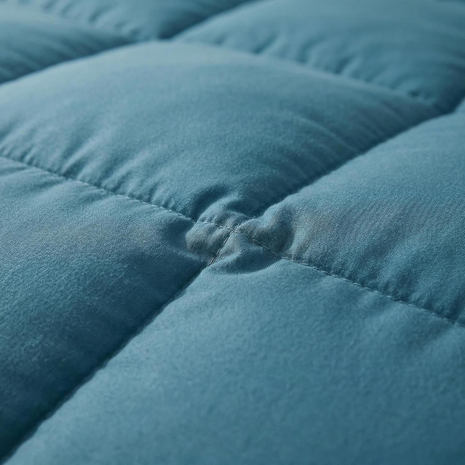Close-up of a soft, blue quilted cotton comforter with square stitching and a central tuft.