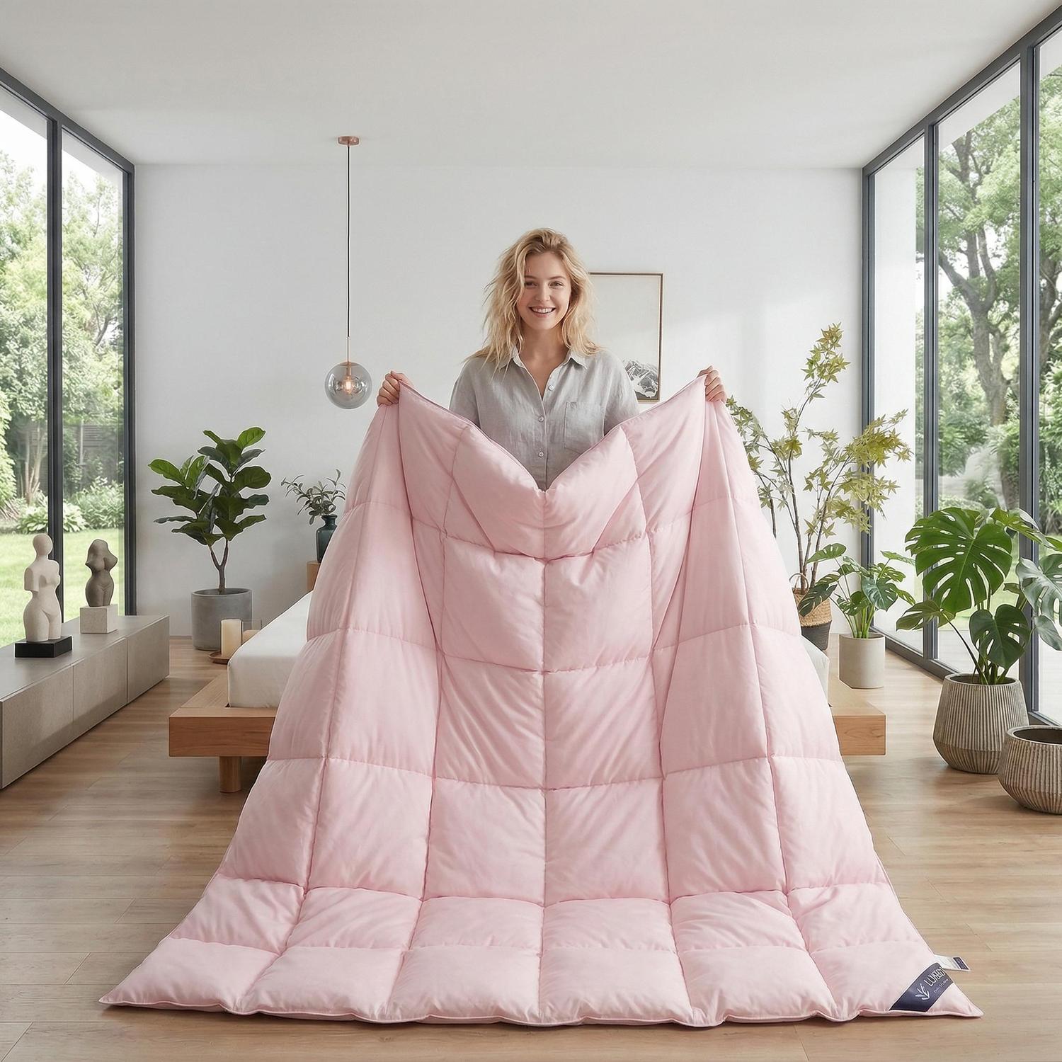 Smiling woman holding a soft pink cotton goose down comforter with a quilted design.