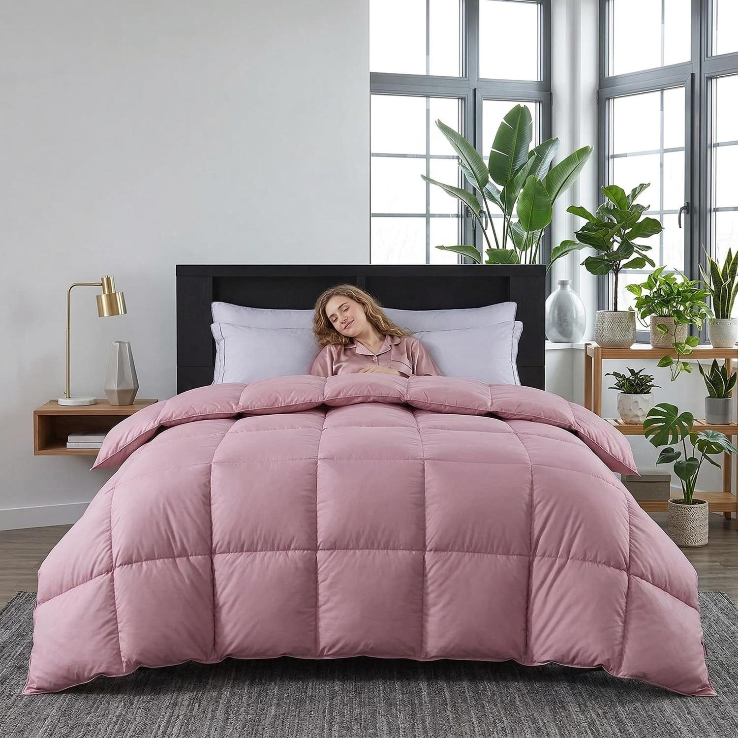 Woman sleeping comfortably under a soft, pink Feather Goose Down Cotton Quilt Comforter in a modern bedroom.
