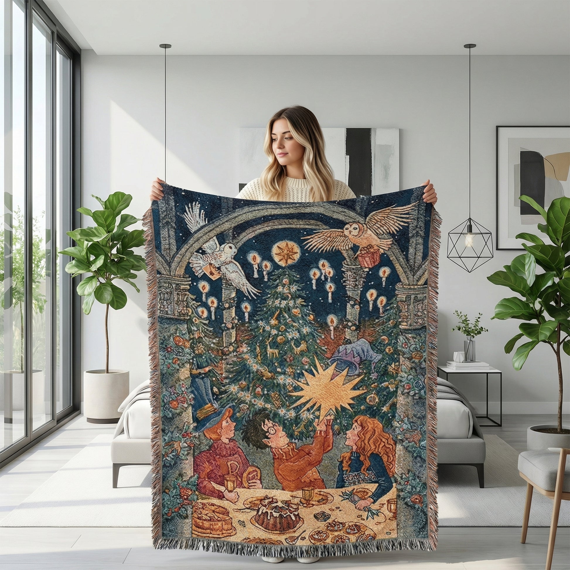 Woman holding a large, dark blue knitted throw blanket with a festive Christmas design, featuring owls, a tree, and people.