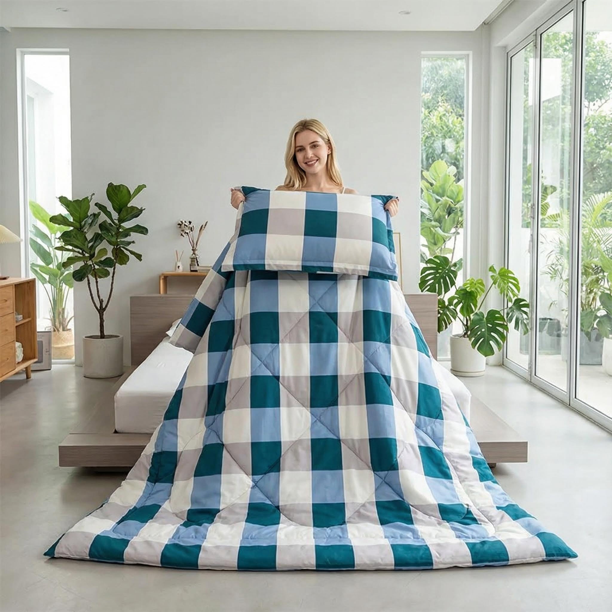 Smiling woman holding a blue, teal, and white plaid flannel fleece blanket and matching pillow in a bright bedroom.