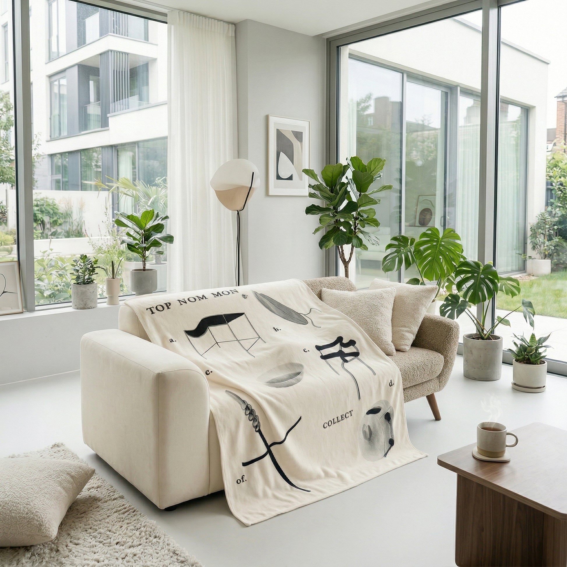 Cream flannel throw blanket with black graphic designs draped over a light beige sofa in a modern living room.