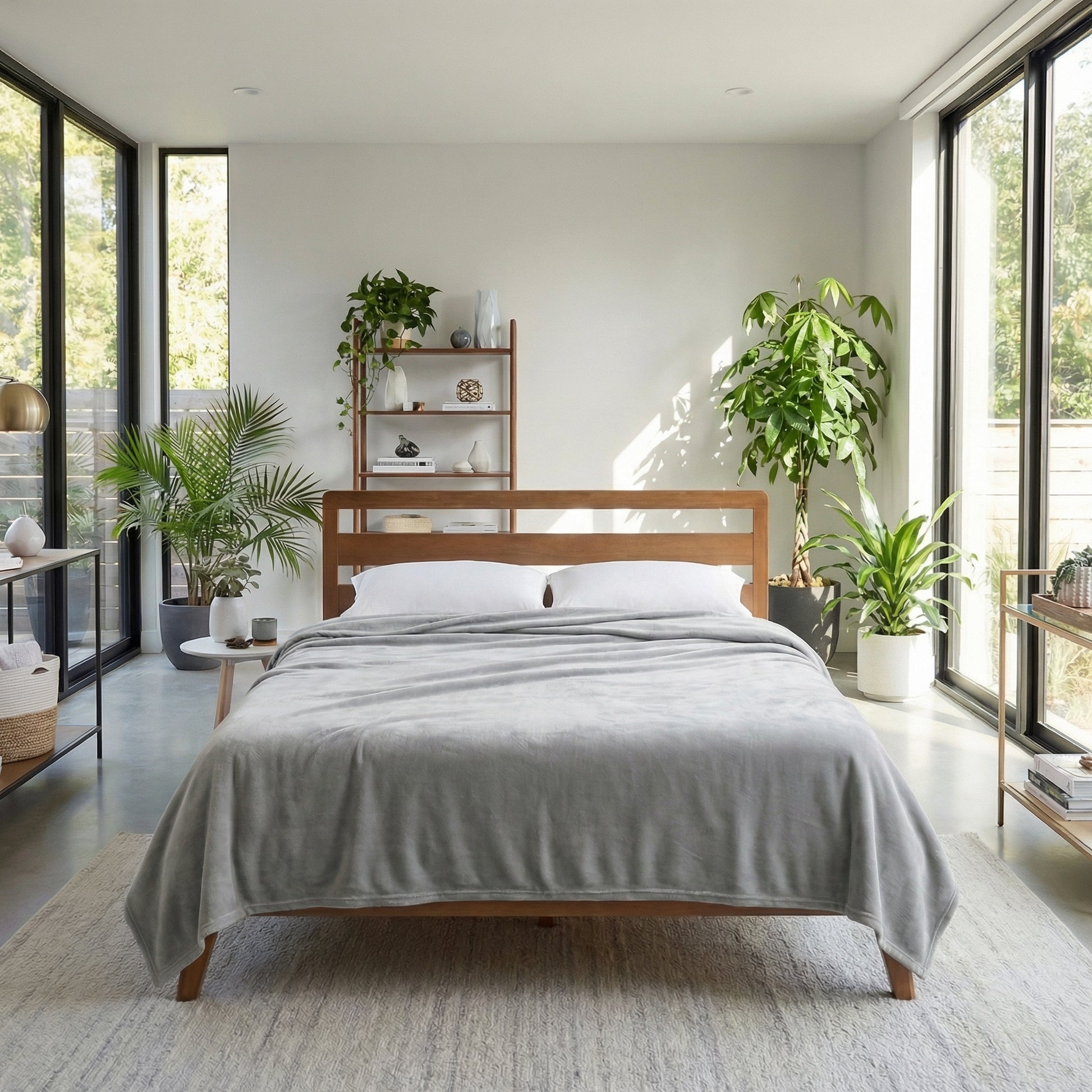Light gray fleece blanket draped over a wooden bed in a bright, modern bedroom with plants.