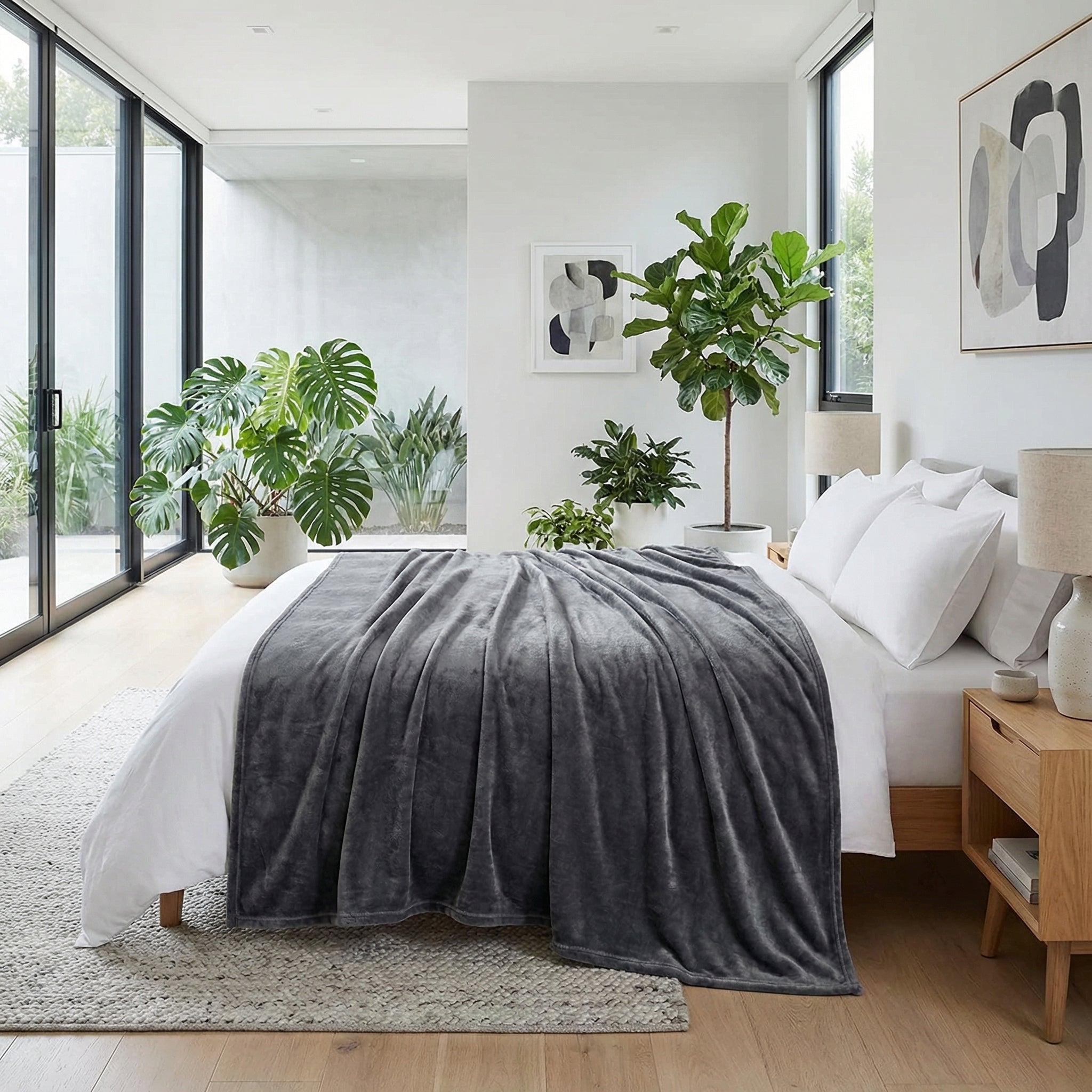 Soft gray fleece blanket draped over a white bed in a modern, plant-filled bedroom.