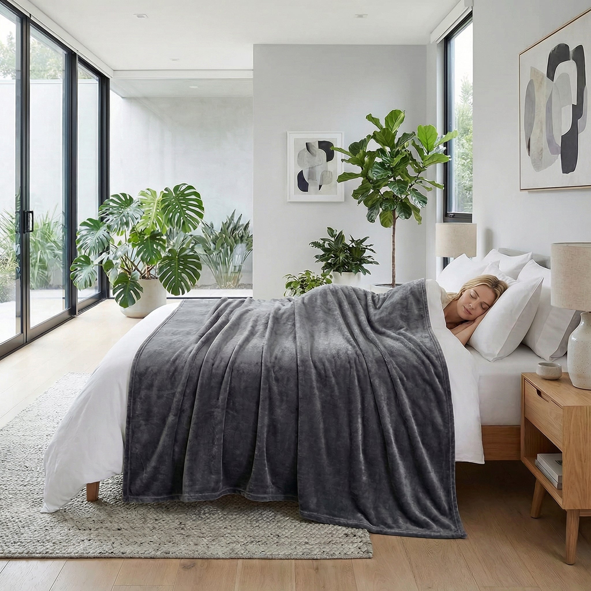Soft gray fleece blanket draped over a woman sleeping in a bright, modern bedroom with plants.
