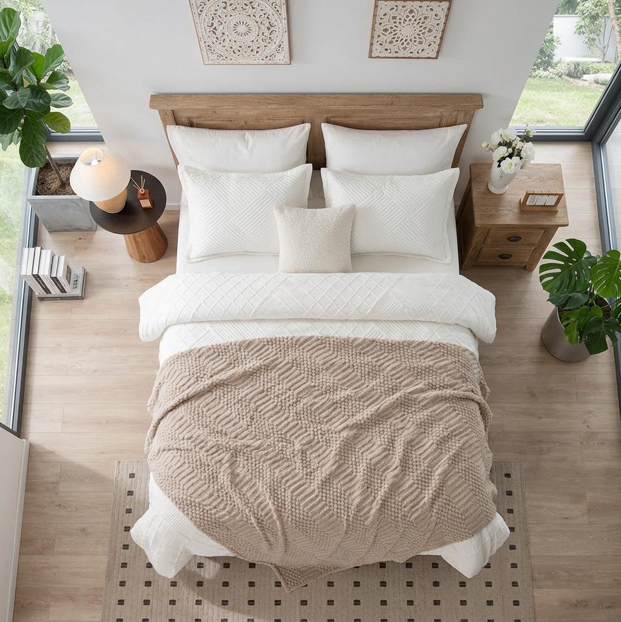 Cozy bedroom with a soft beige 50x70 inch fleece throw blanket draped over a white bed, surrounded by plants.