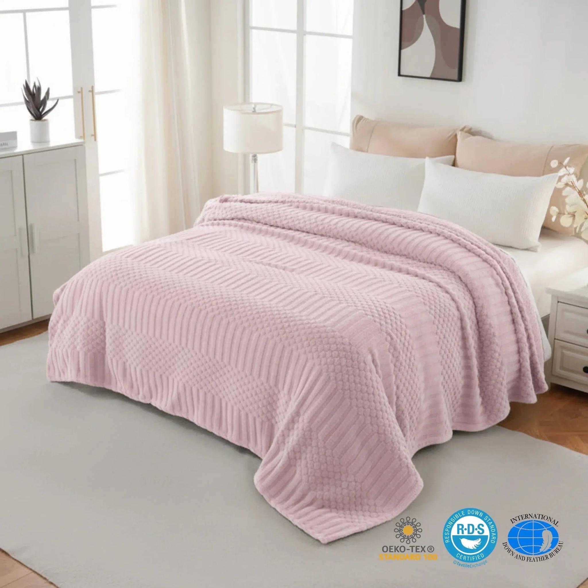 Soft pink fleece throw blanket with textured geometric patterns draped over a bed.