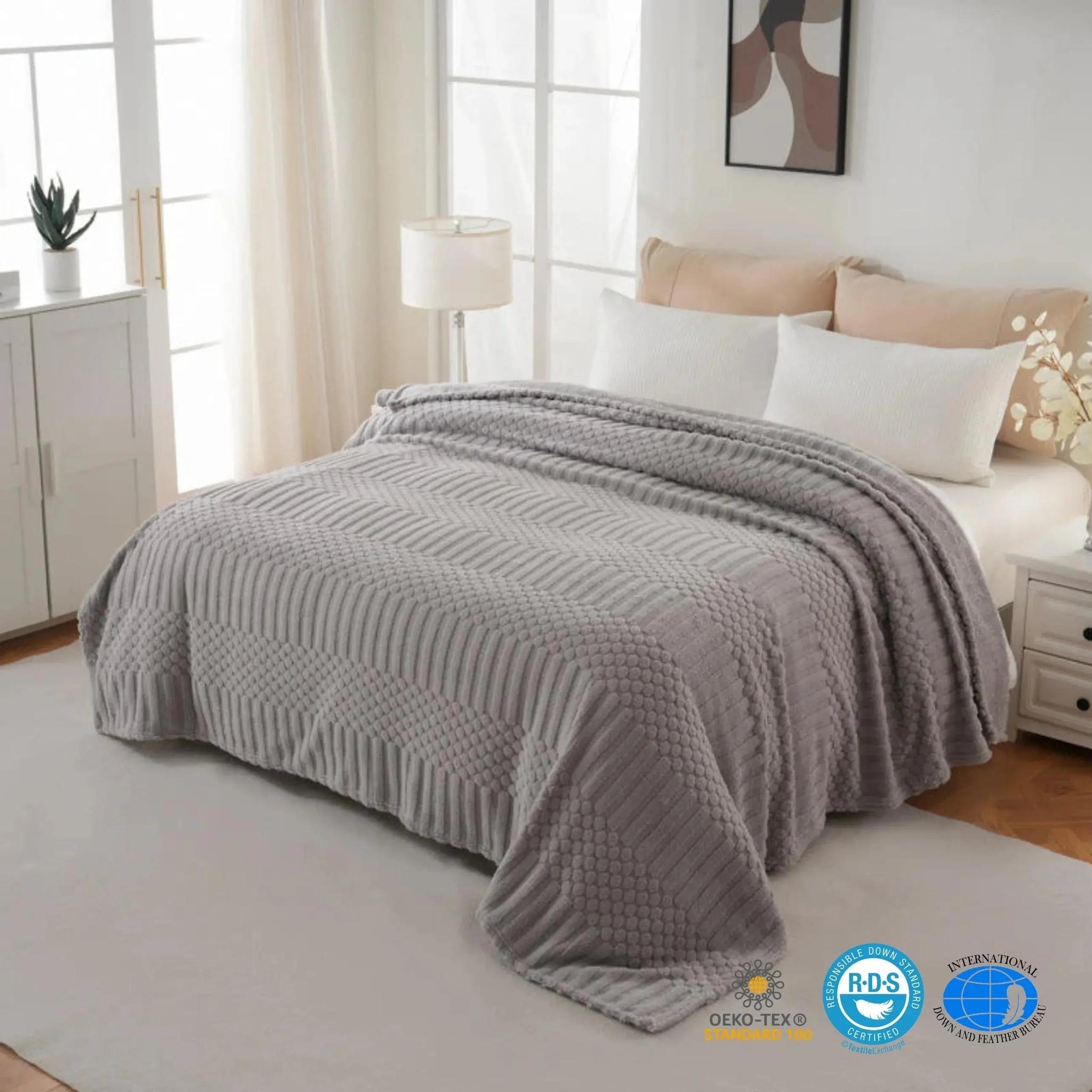 Soft gray fleece throw blanket with textured geometric patterns draped on a bed.