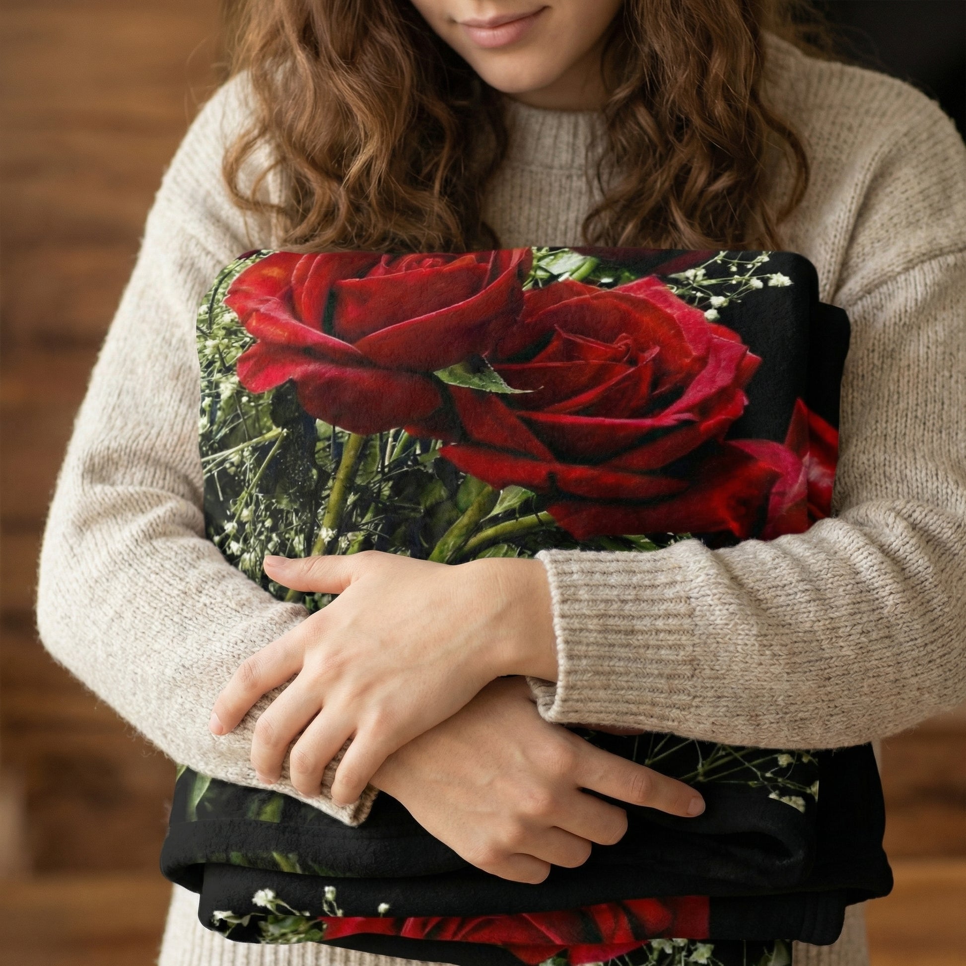 Woman holding a folded black fleece blanket with a vibrant 3D print of red roses and babysbreath.