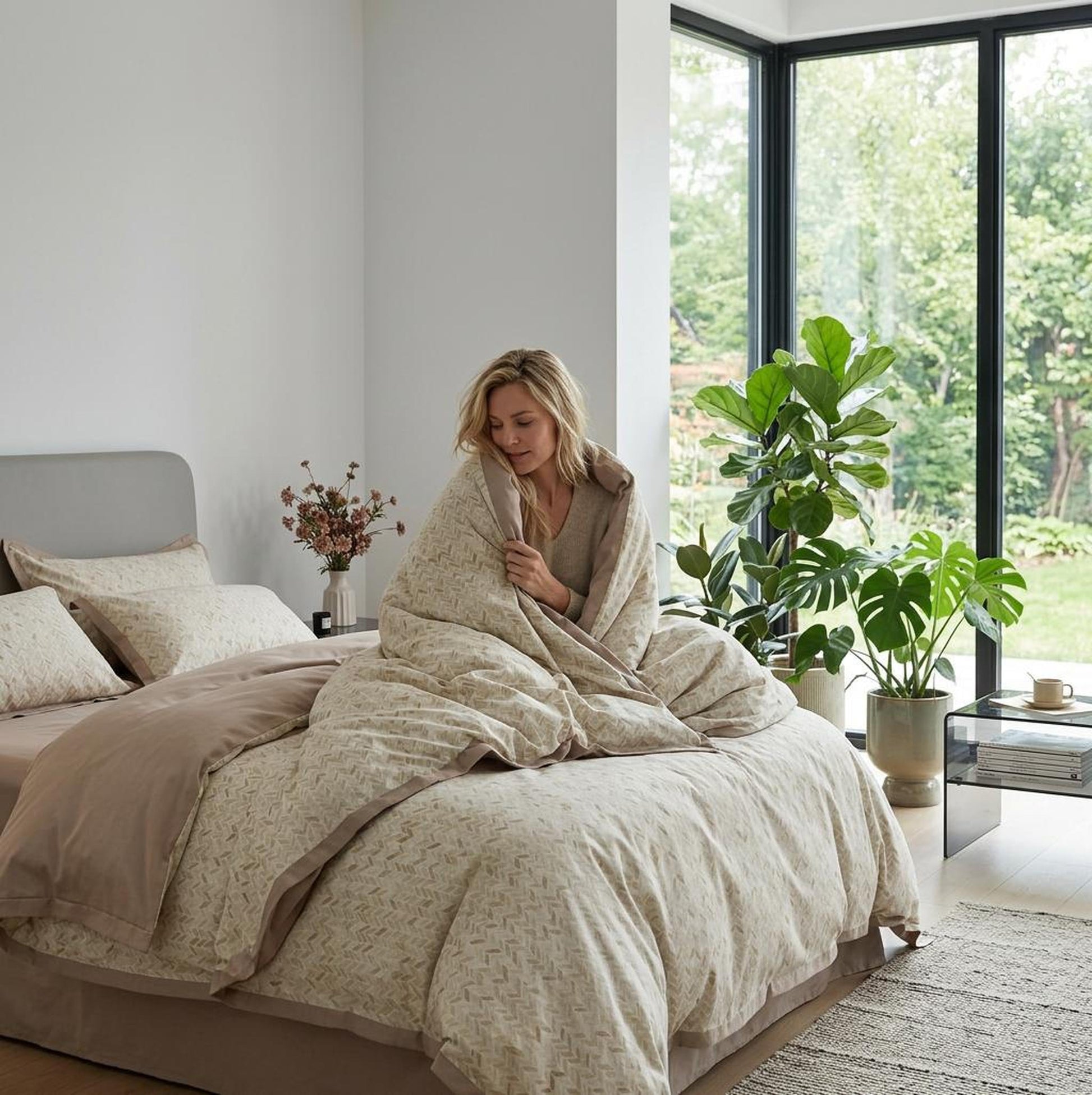 Woman wrapped in a beige floral microfiber duvet cover set on a bed in a bright bedroom.