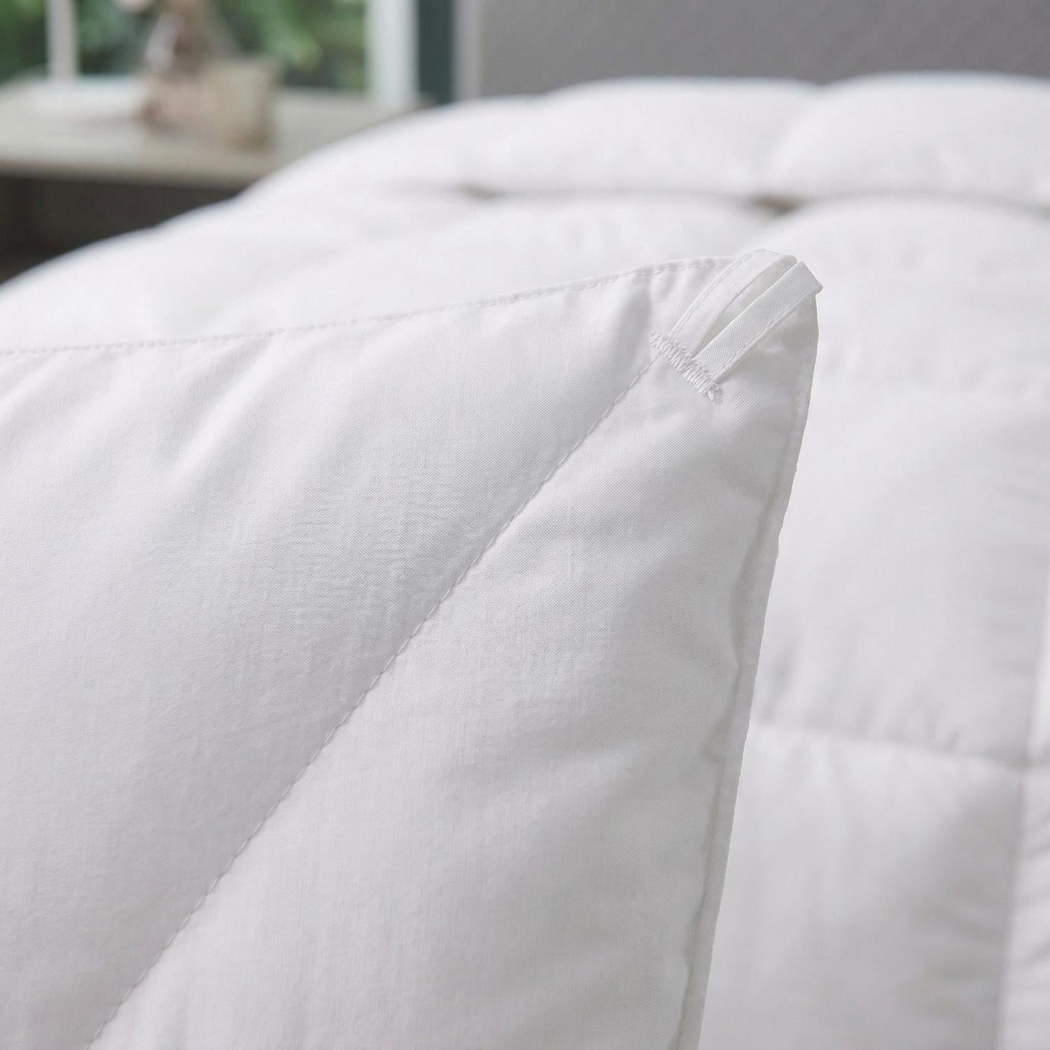 Close-up of a fluffy white quilted duvet comforter with corner loops, showing soft cotton-polyester material.