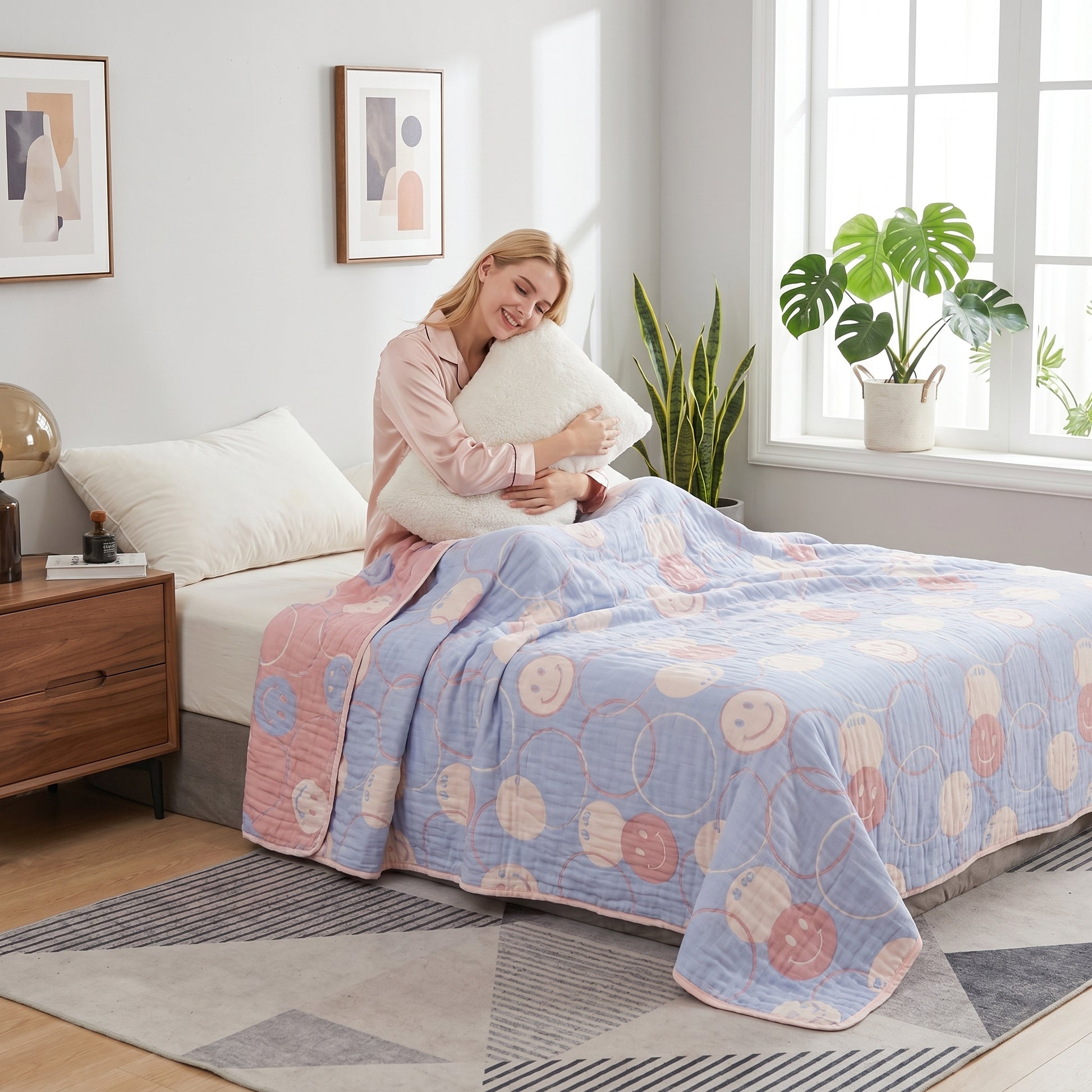 Woman on bed with a reversible blue and pink 6-layer cotton gauze blanket featuring a smiley face pattern.