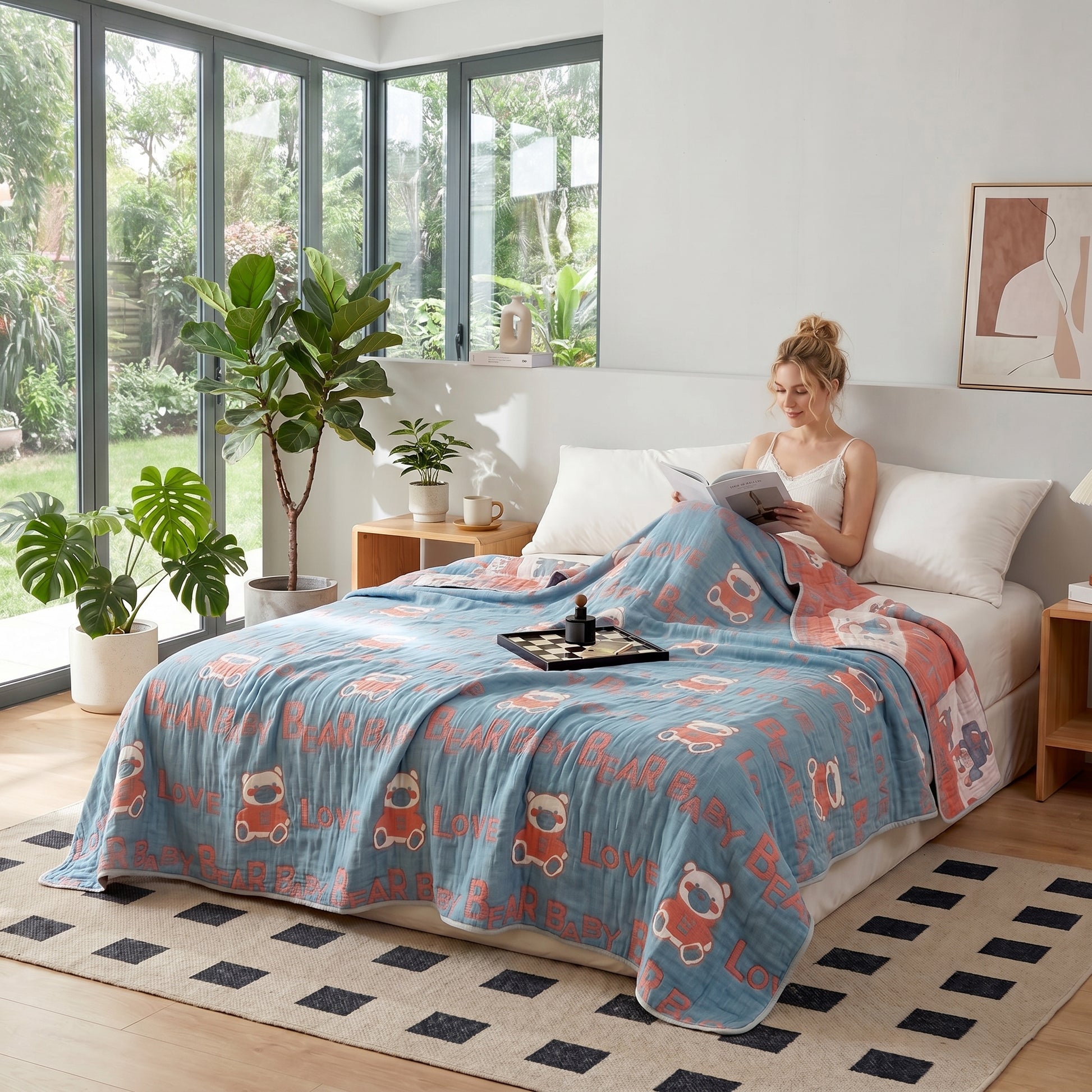 Woman relaxing in bed with a blue and peach 6-layer cotton gauze blanket featuring bear and "LOVE" patterns.