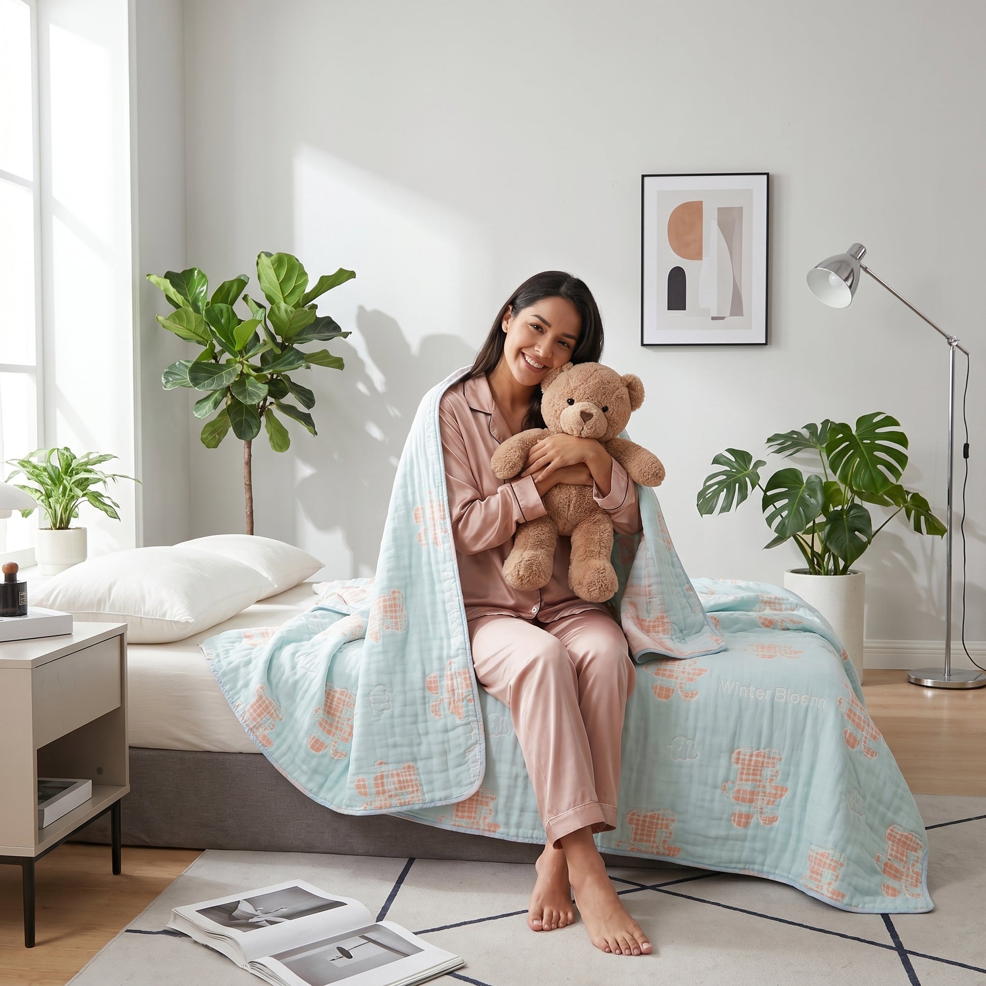 Smiling woman in pink pajamas holding a teddy bear, covered by a light blue 6-layer cotton gauze blanket with bear patterns.