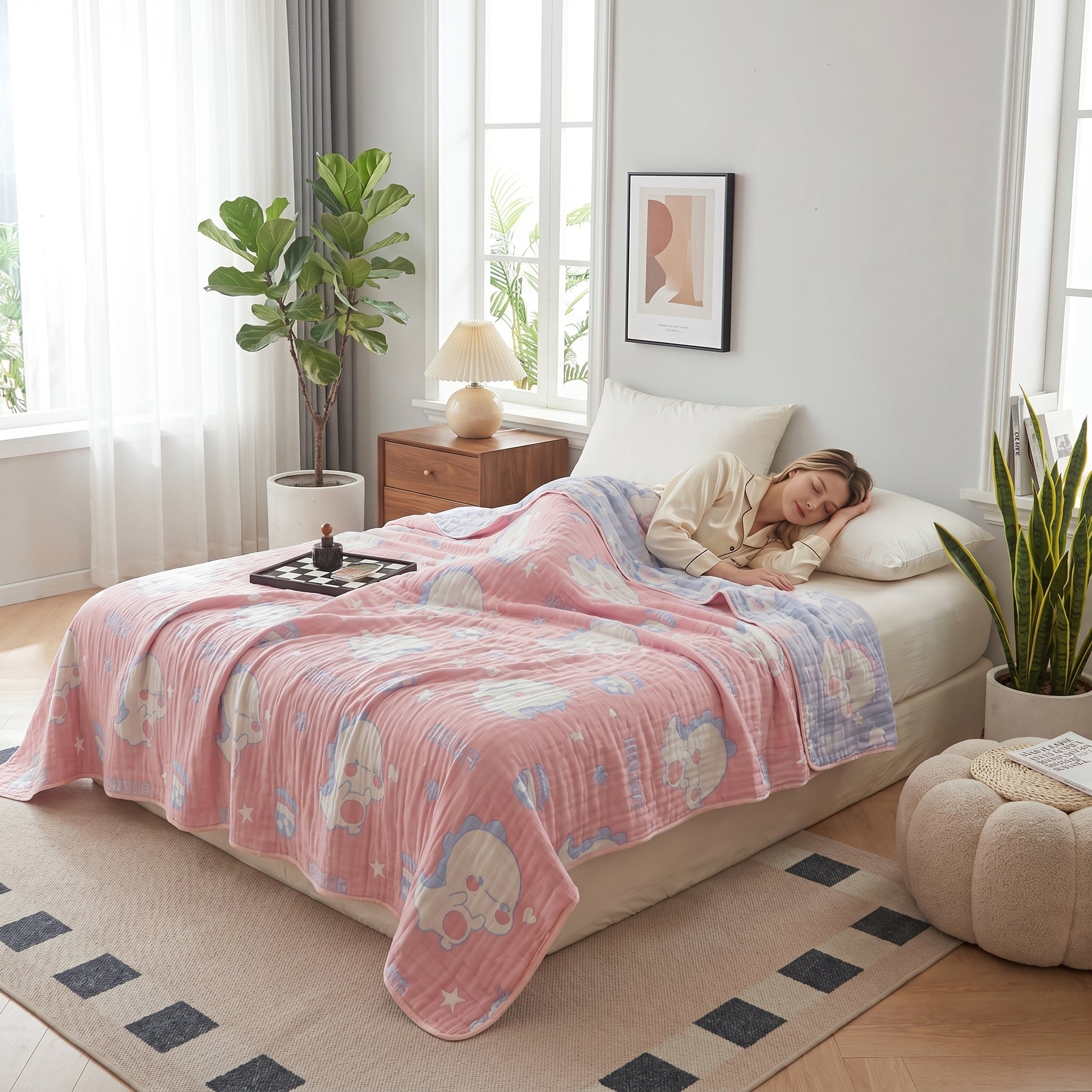 Pink and blue reversible 6-layer cotton gauze blanket with cute animal print on a bed with a sleeping person.