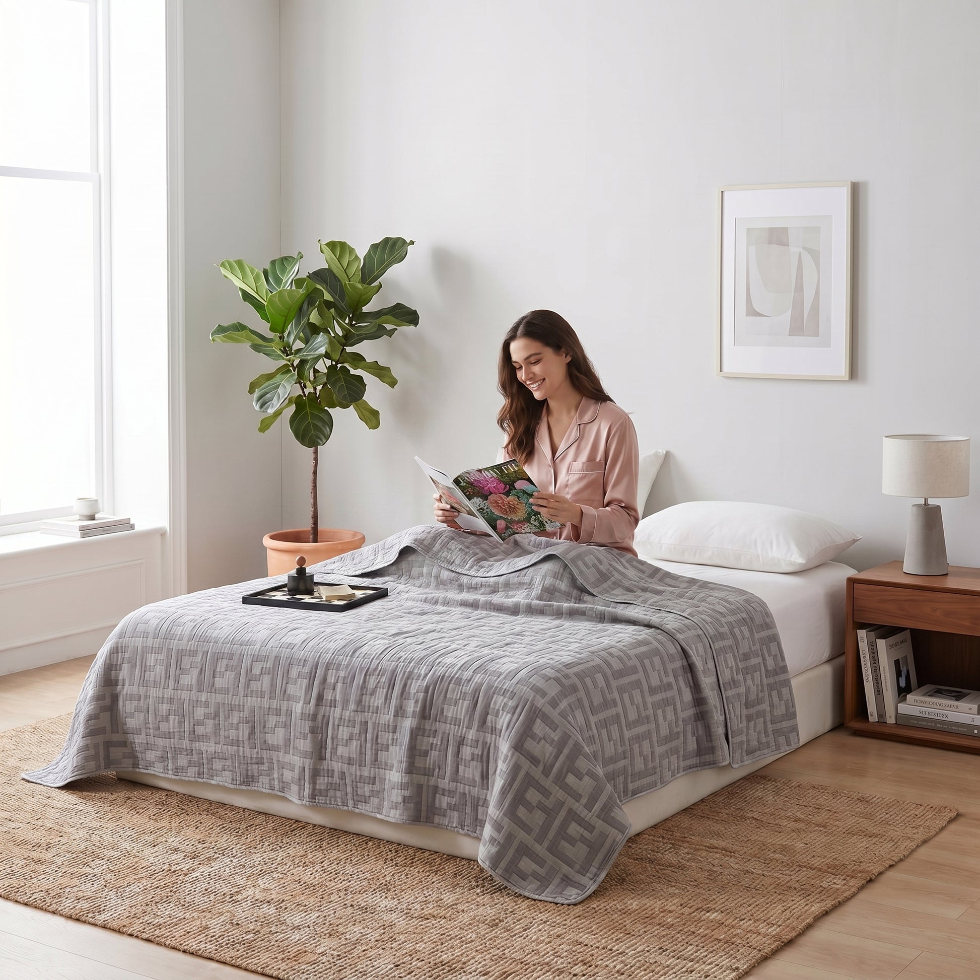 Woman on bed with a grey 6-layer cotton gauze blanket featuring a geometric pattern, reading a magazine.
