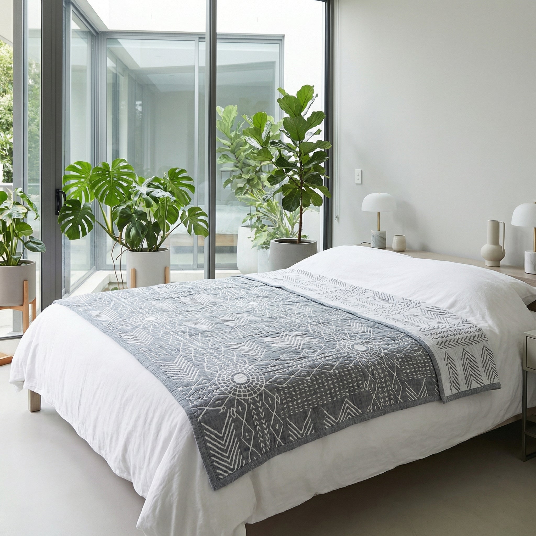 Grey three-layer gauze cotton towel blanket with white geometric patterns on a white bed in a modern bedroom.