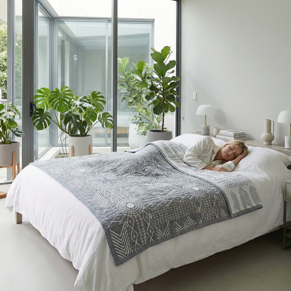 Woman sleeping peacefully under a gray three-layer gauze cotton towel blanket with white geometric patterns in a bright bedroom.