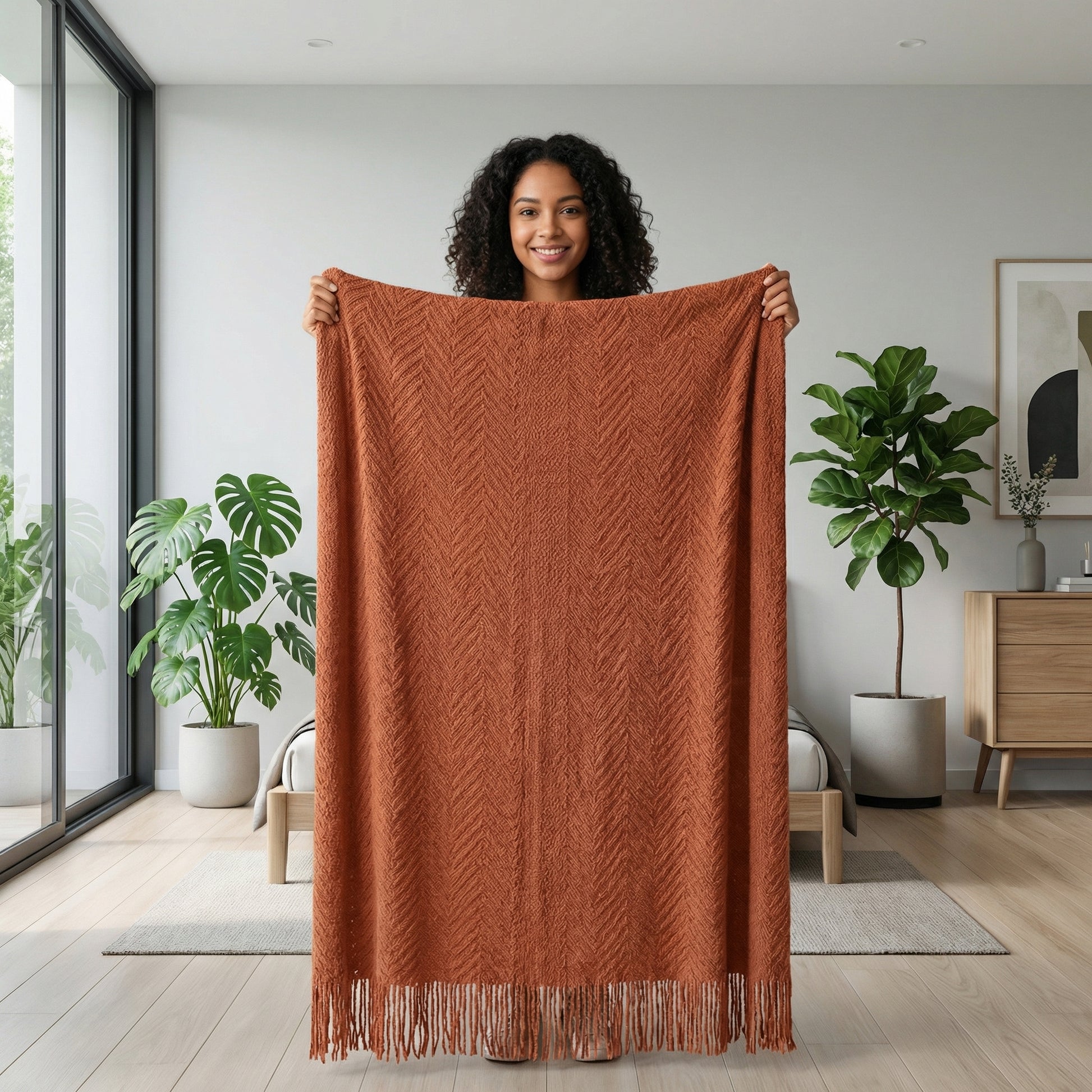Smiling woman holding up a large, textured terracotta throw blanket with a geometric pattern and fringe.