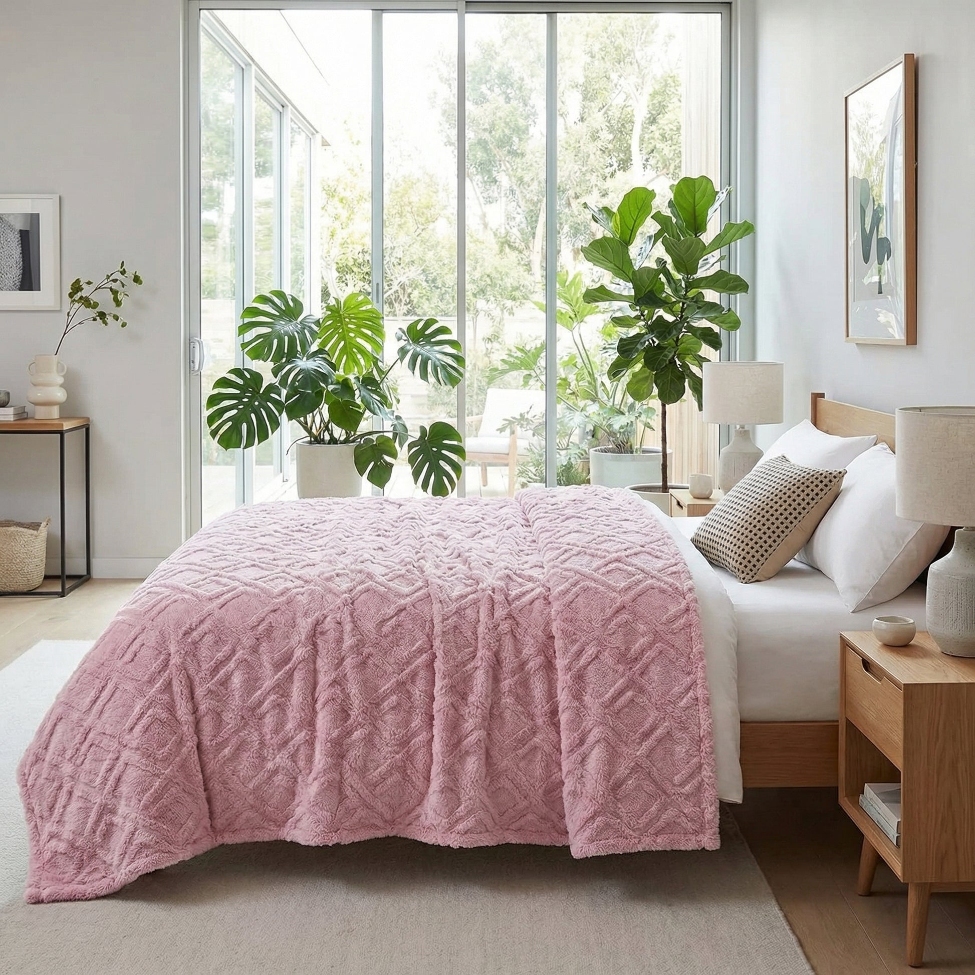 Pink plush fleece blanket with a geometric pattern draped over a bed in a bright bedroom.