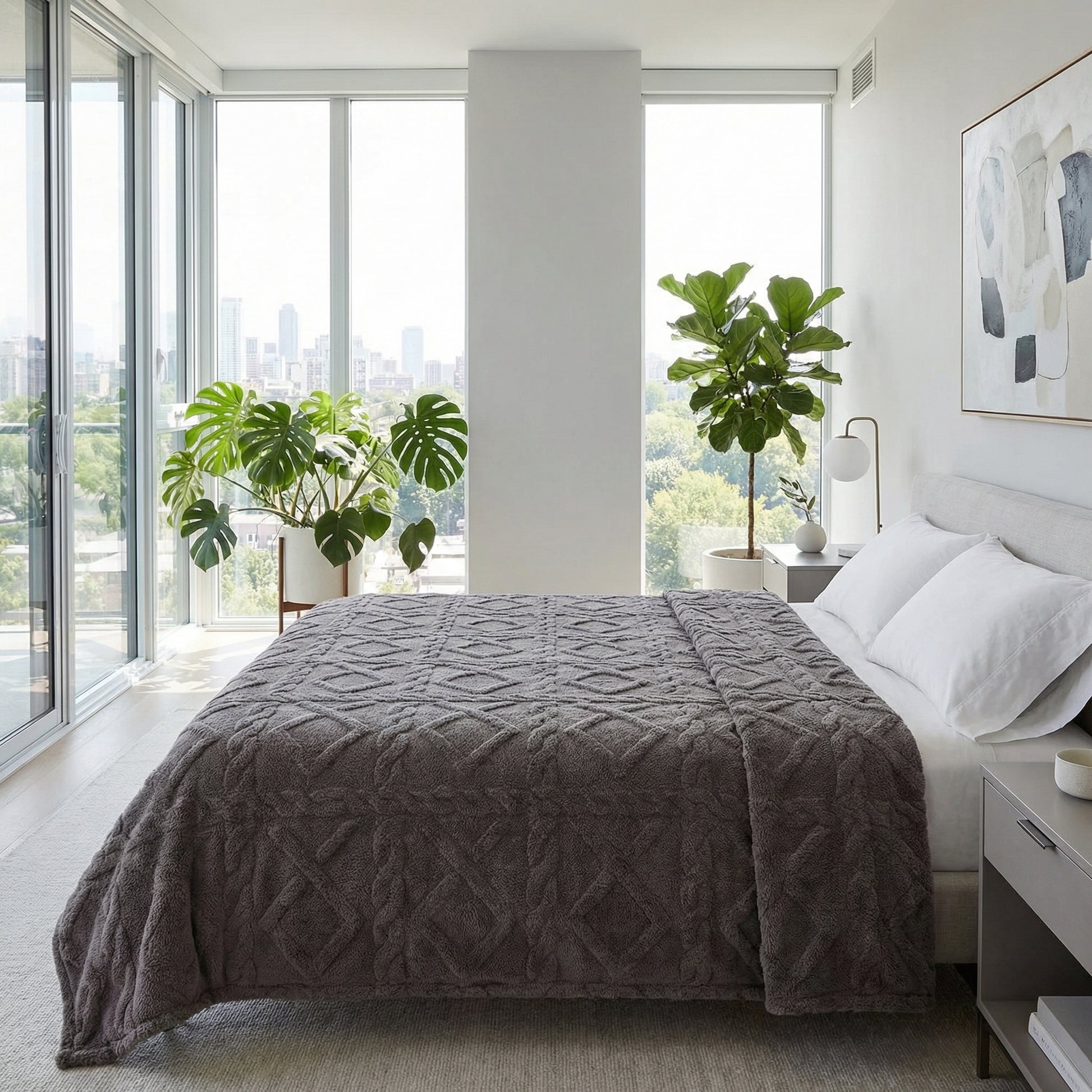 Soft gray geometric pattern fleece blanket draped on a bed in a modern bedroom with large windows.