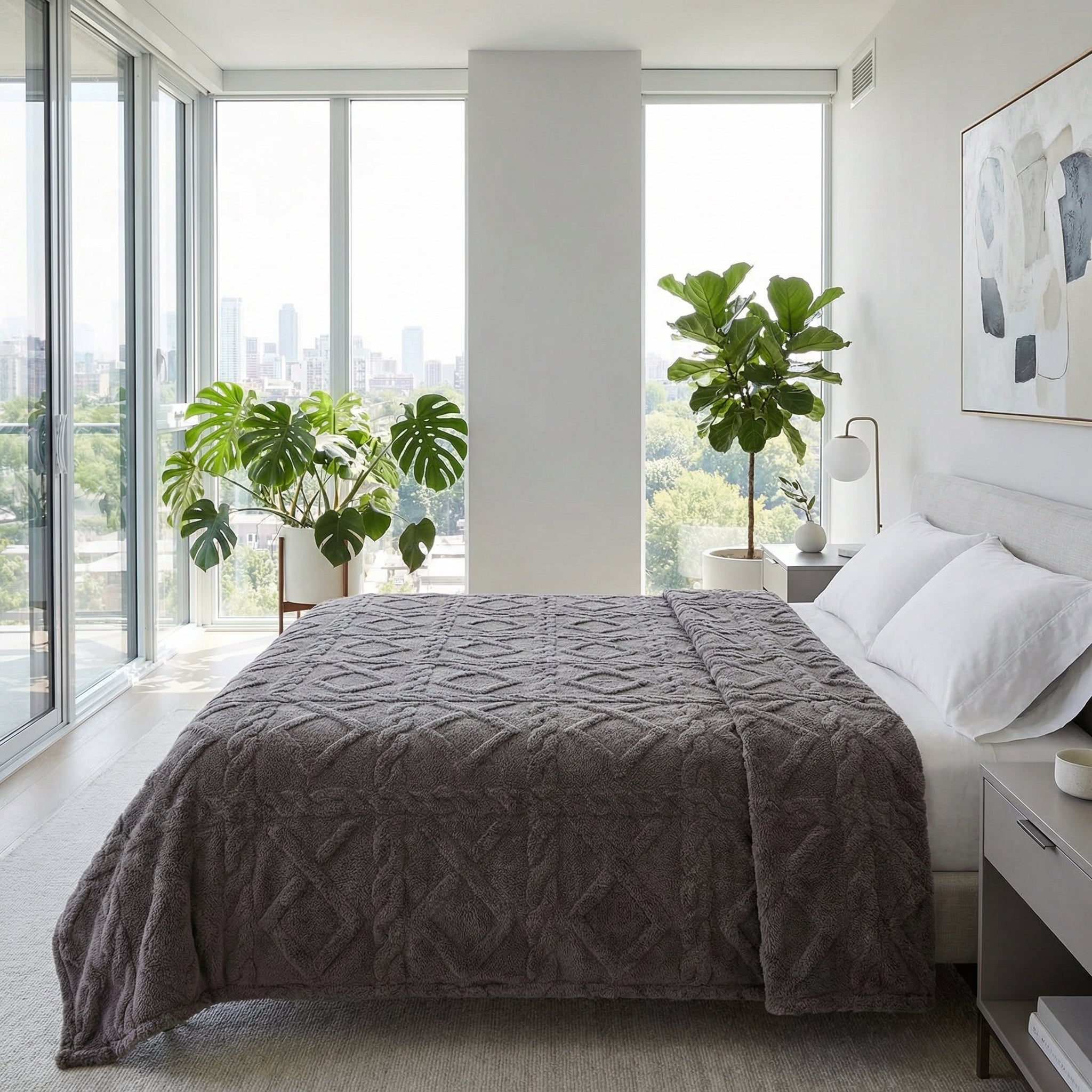 Soft gray geometric pattern fleece blanket draped on a bed in a modern bedroom with large windows.