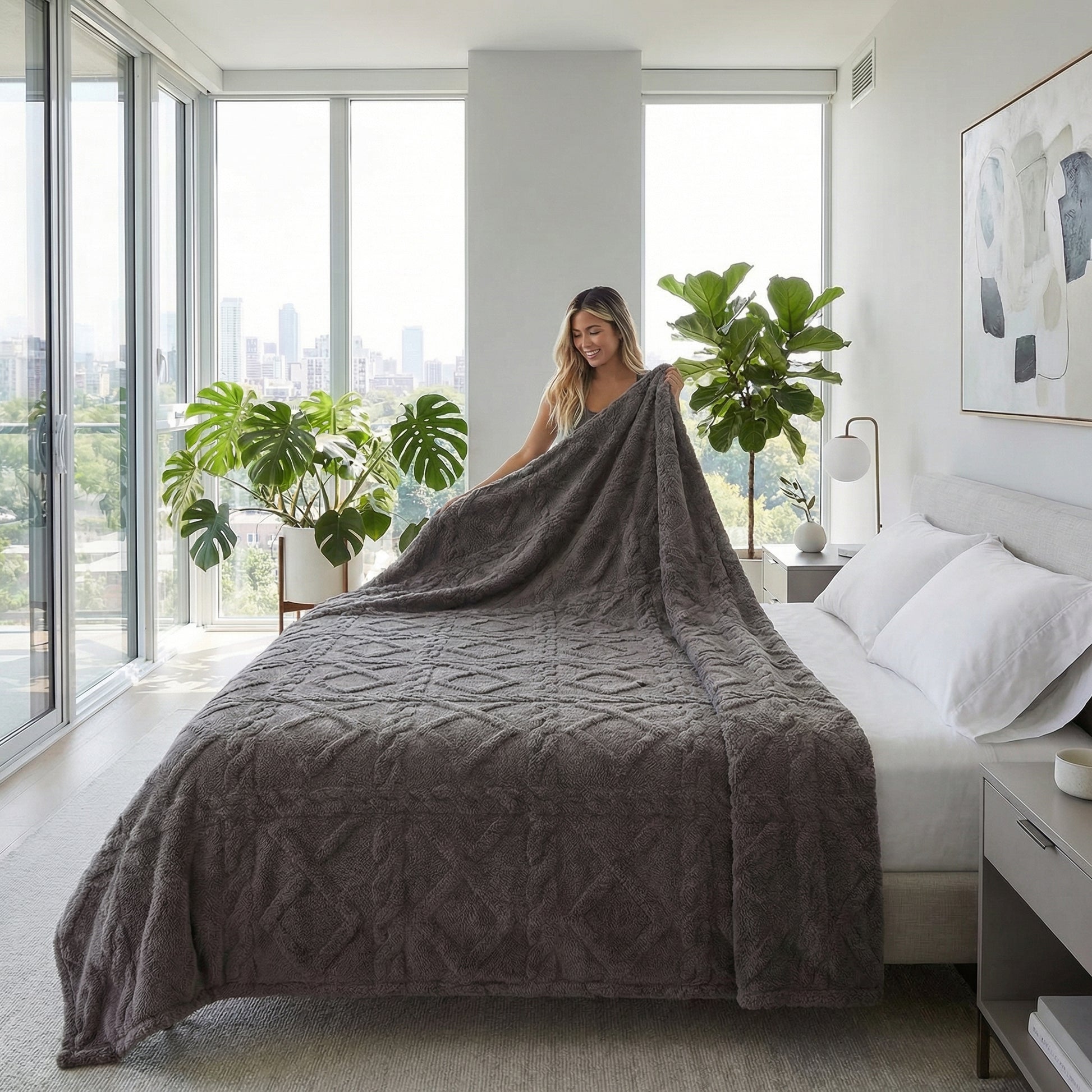 Woman placing a soft, dark gray geometric pattern fleece blanket on a bed in a bright, modern bedroom.