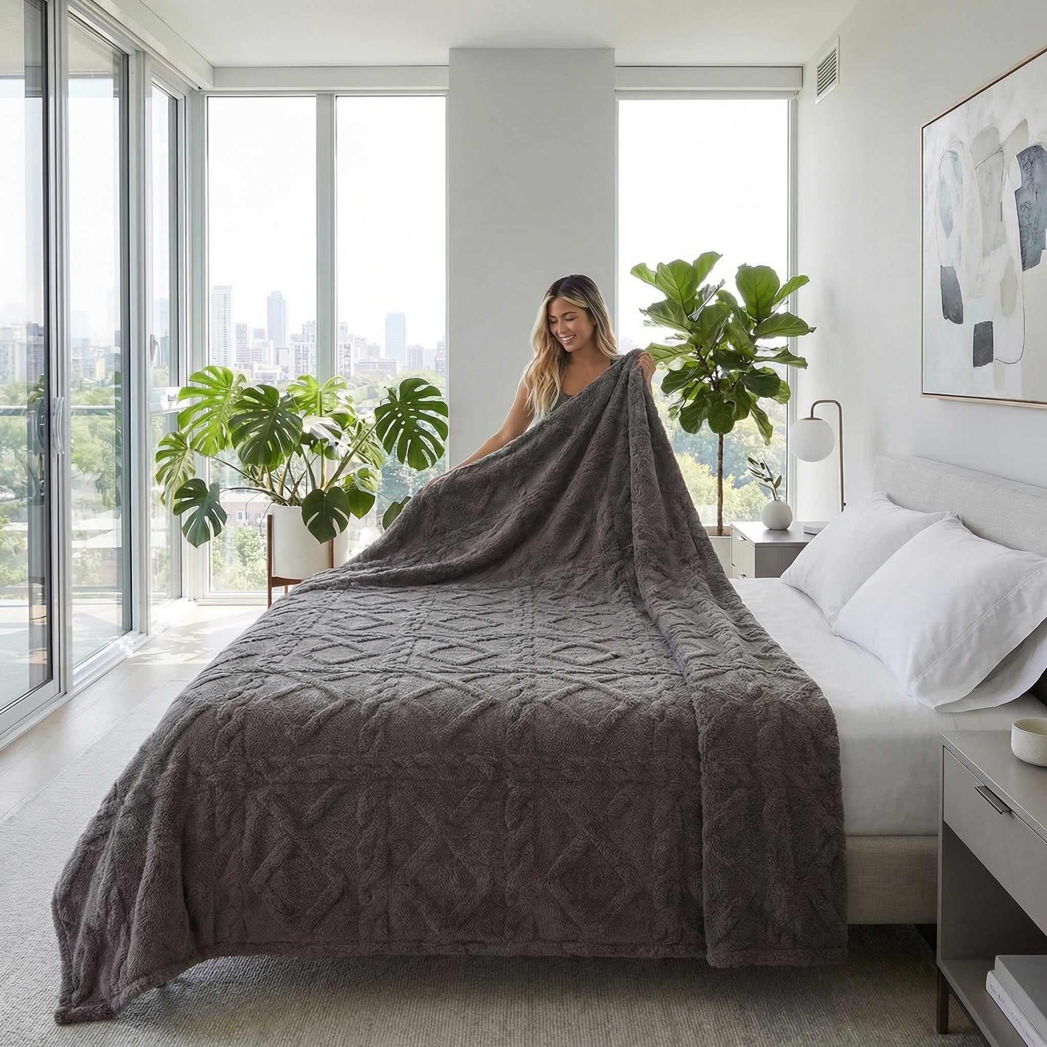 Woman placing a soft, dark gray geometric pattern fleece blanket on a bed in a bright, modern bedroom.