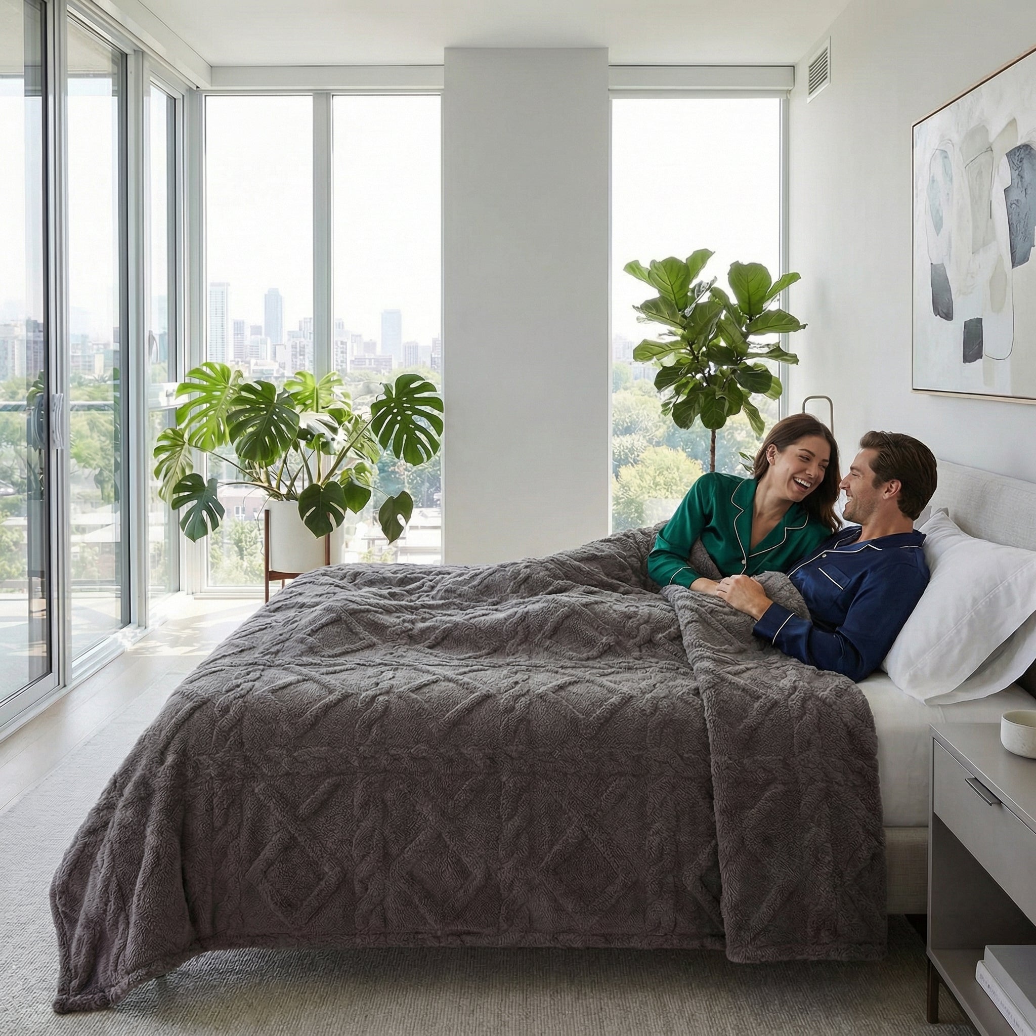 Gray geometric pattern fleece blanket covering a couple relaxing in a modern bedroom with city views.