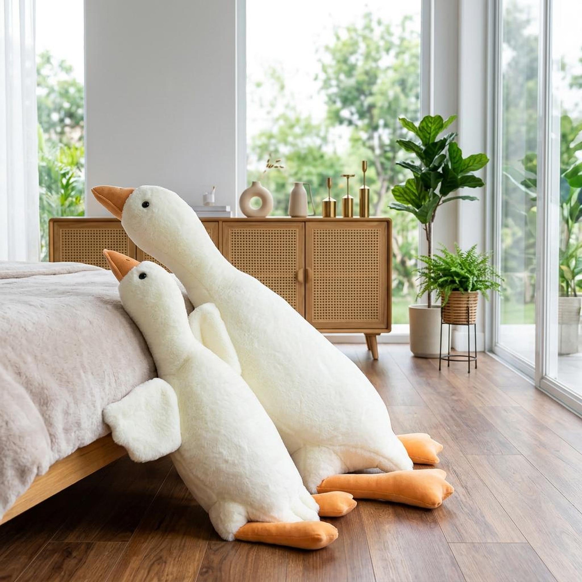 Two large white goose plush pillow toys leaning against a bed in a modern bedroom.