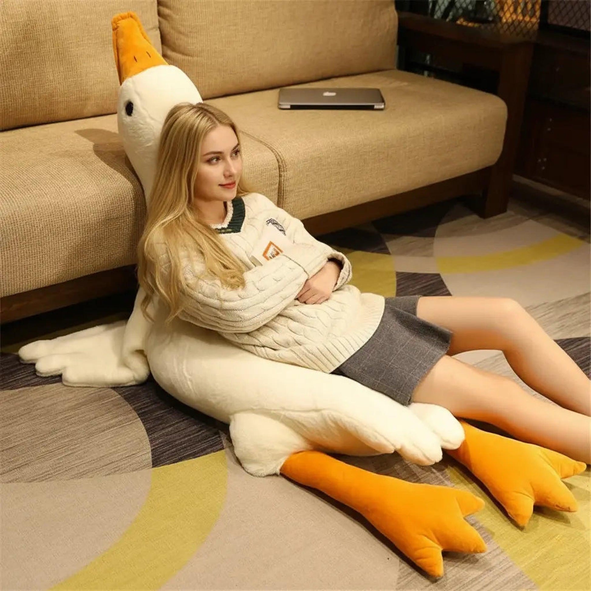 Woman leaning on a large white goose plush pillow toy with orange beak and feet.
