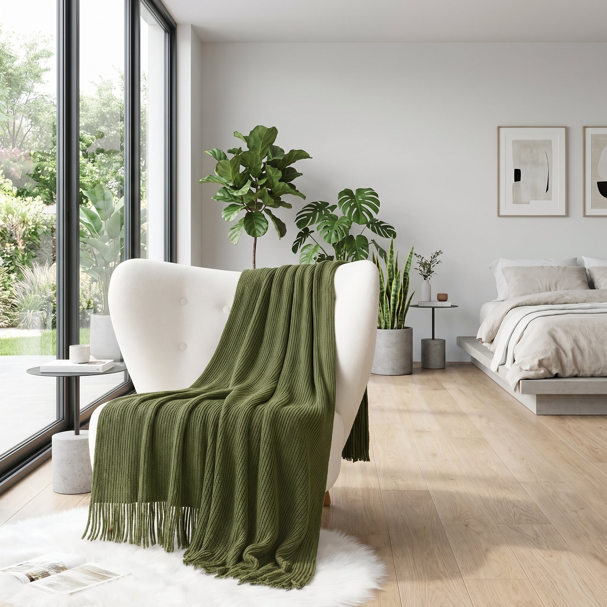 Green chenille knit throw blanket draped over a white armchair in a modern bedroom with large windows.
