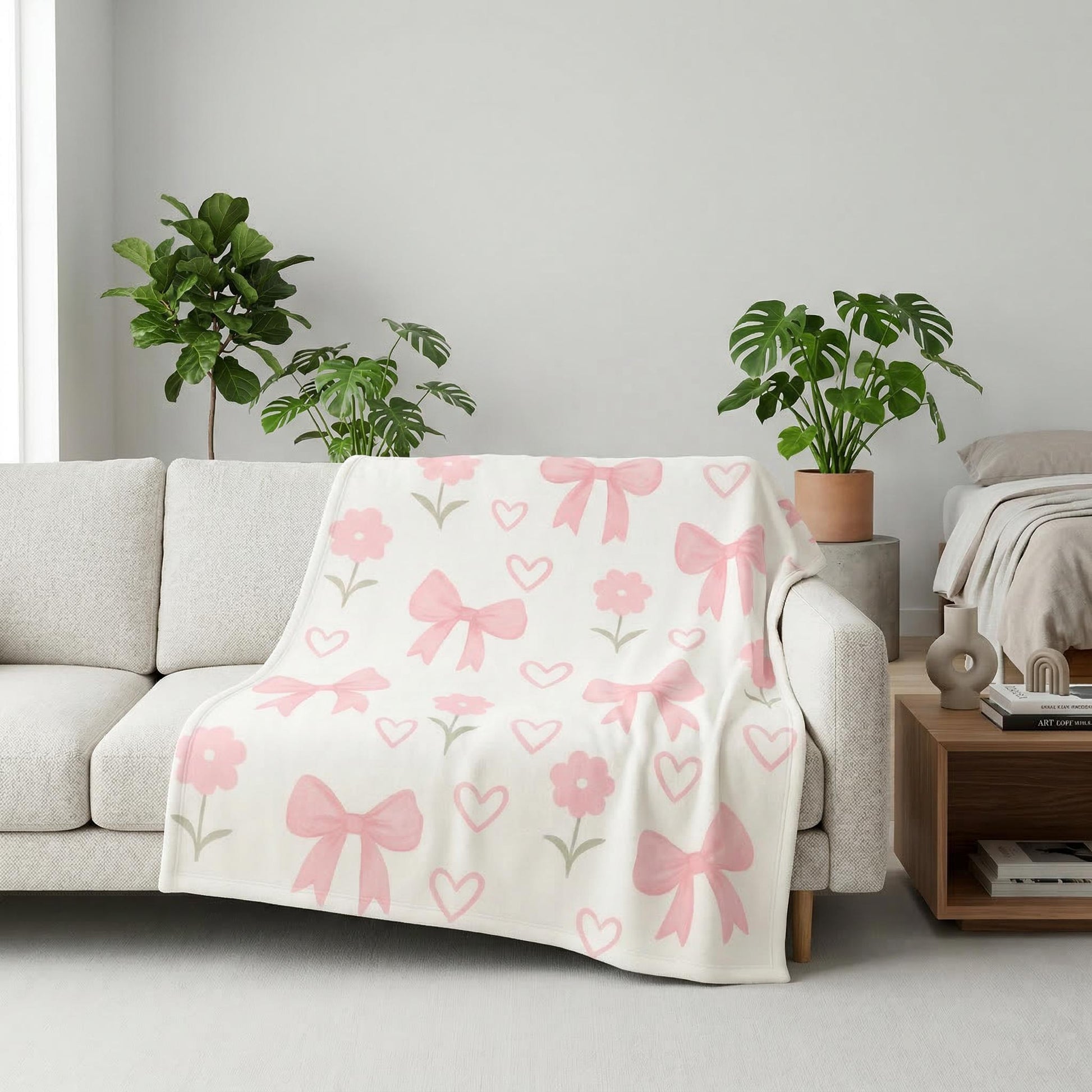 White flannel blanket with a pattern of pink bows, hearts, and flowers draped over a light sofa.