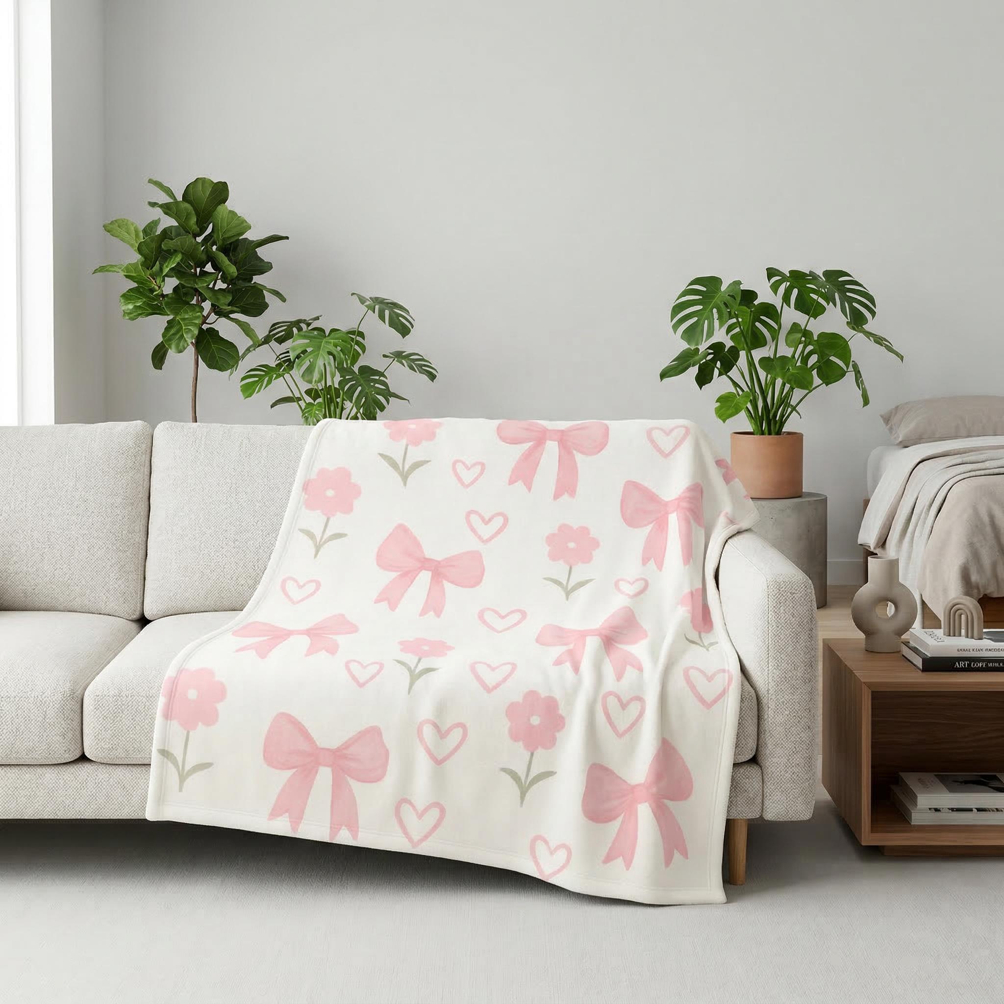 White flannel blanket with a pattern of pink bows, hearts, and flowers draped over a light sofa.