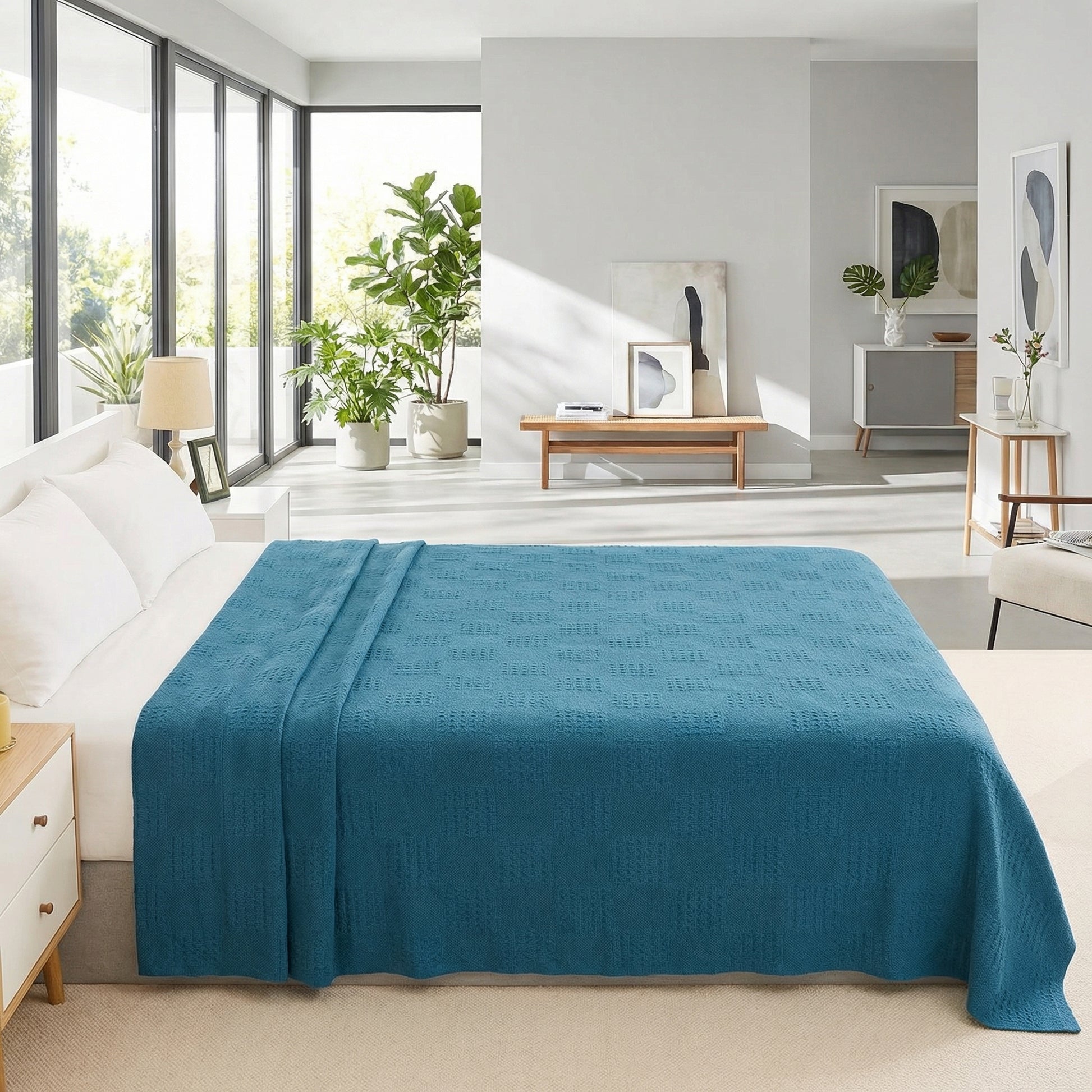 Teal hollow knit cotton summer blanket draped over a bed in a bright, modern bedroom.